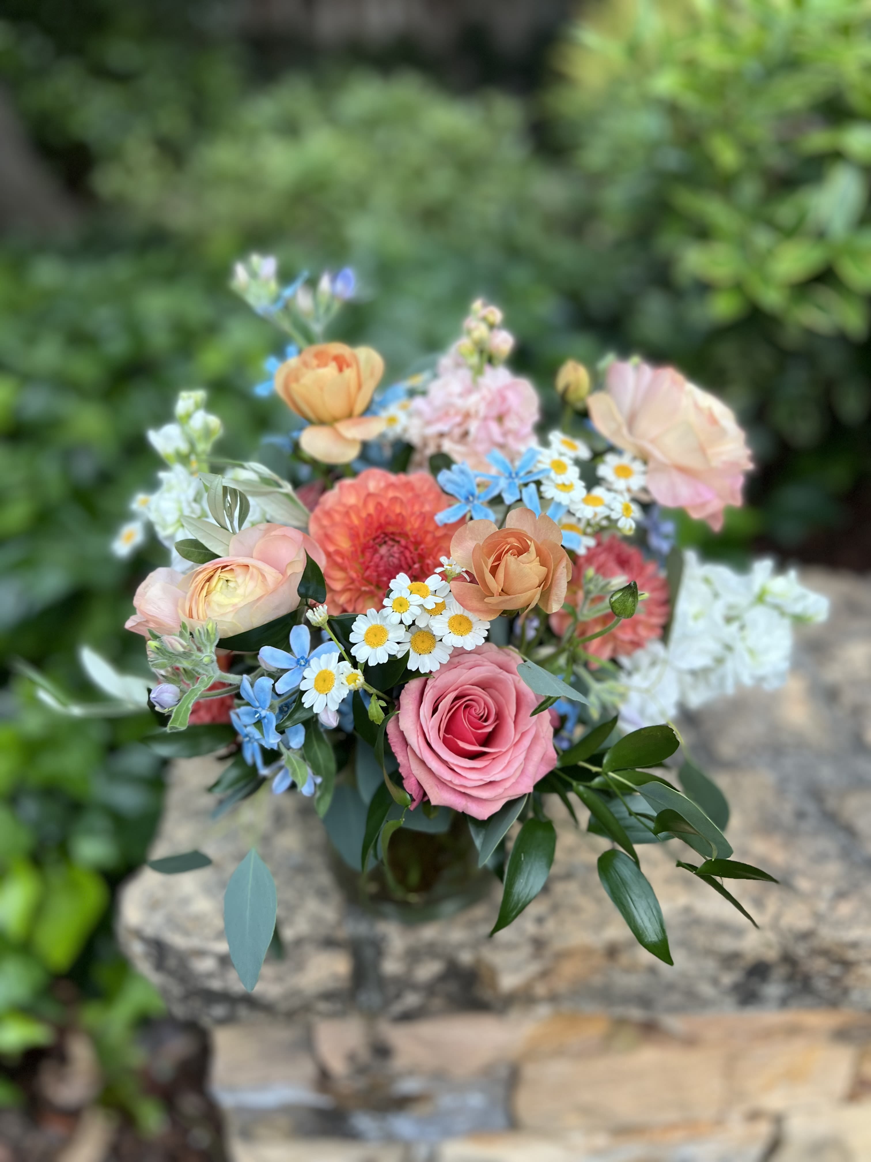Mixed bouquet of pink, peach, and blue flowers in a glass vase