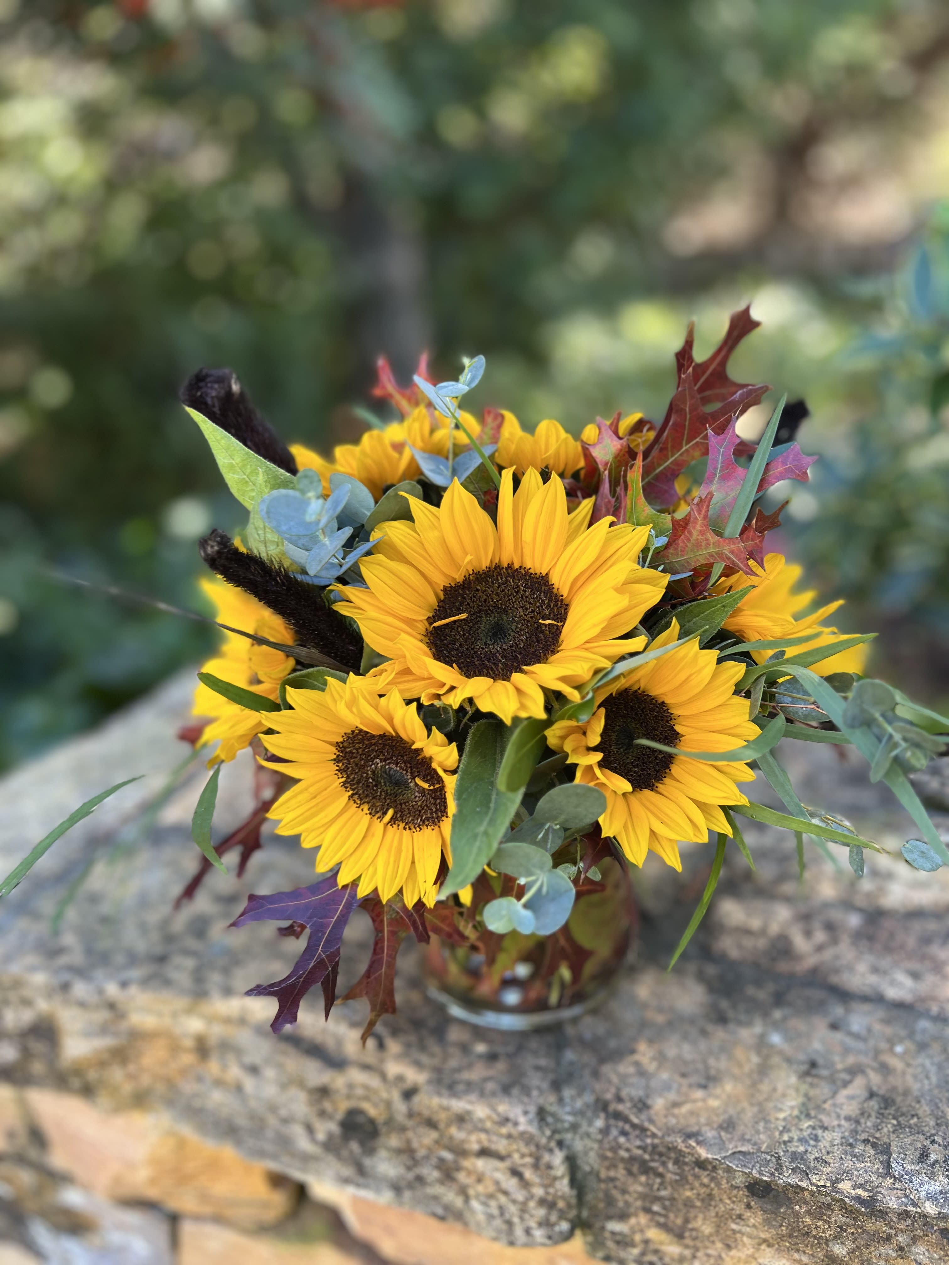 Bouquet of yellow sunflowers with autumn leaves in a glass vase