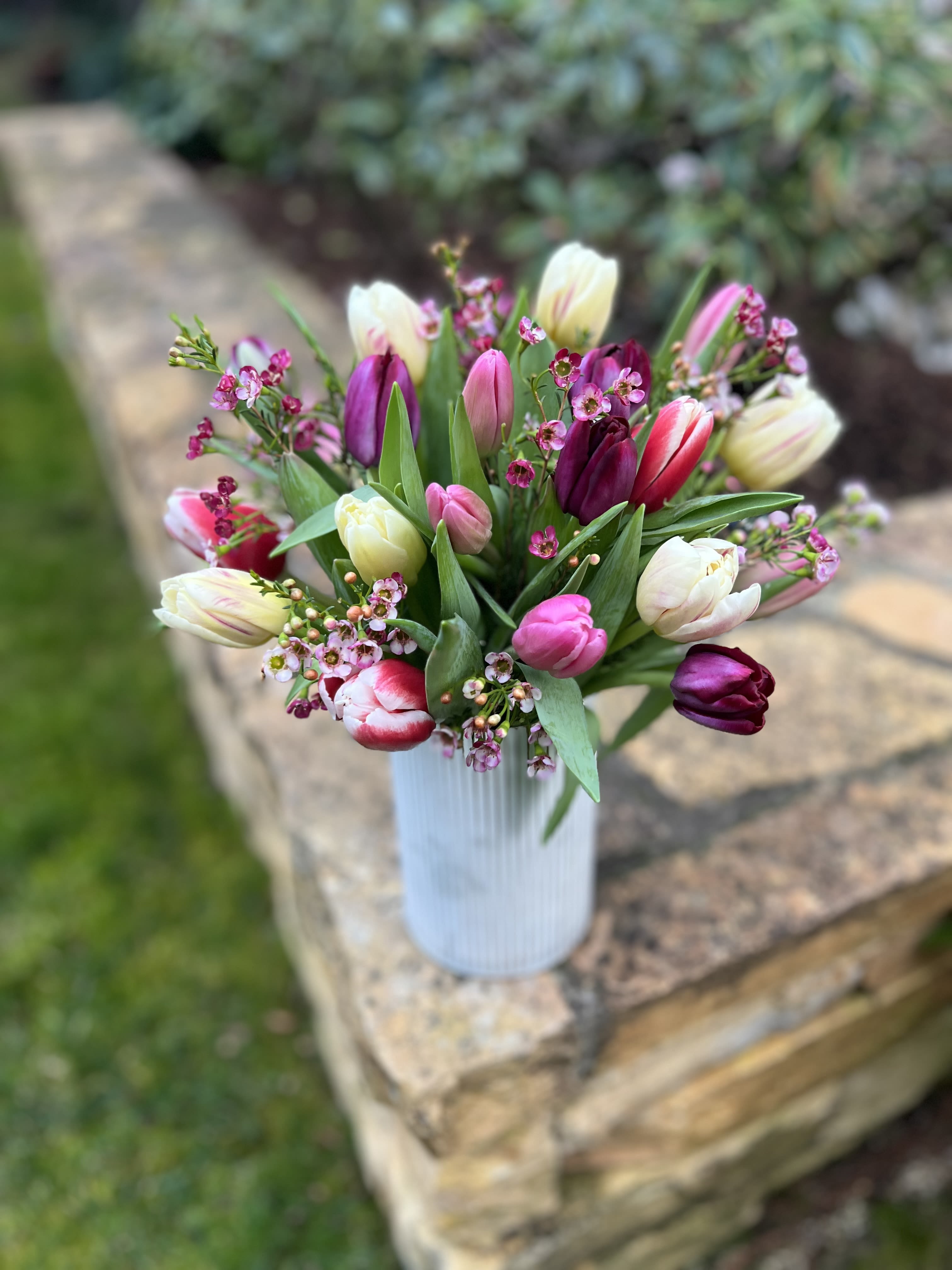 Springtime Tulips  - Send these Spring time beauties to any tulip lover and they’ll surely love them! Assorted tulips in seasonal colors arranged in a tall white rustic container and seasonal filler. 