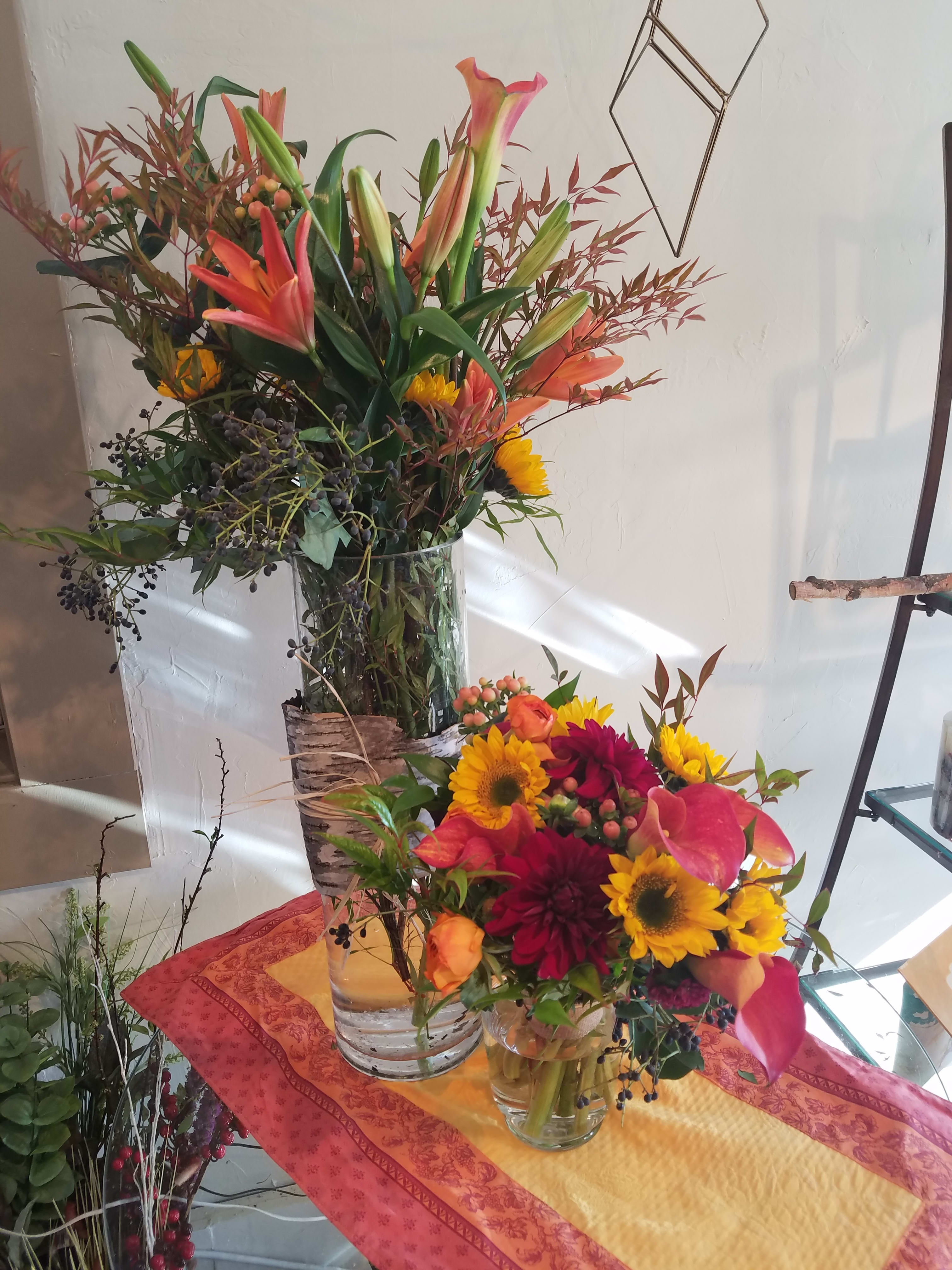 Two colorful floral arrangements in clear glass vases, one tall and one low.