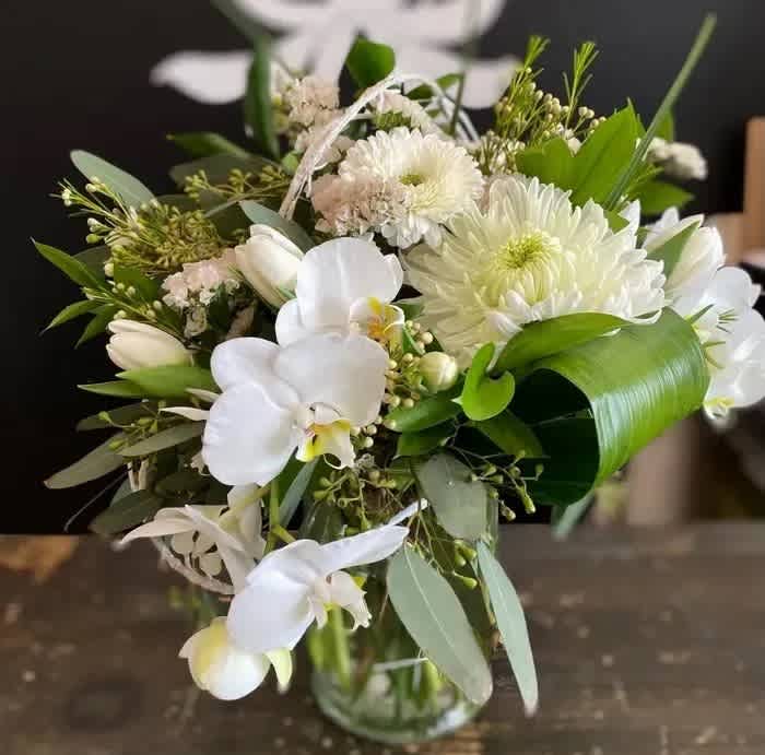 White floral bouquet in a glass vase with orchids and daisies