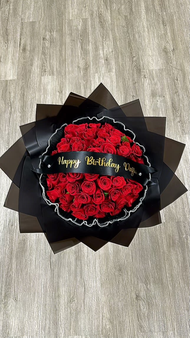 Birthday Cascade Bouquet - Make a bold statement with this stunning bouquet of 25 premium roses, elegantly wrapped in sleek black paper and finished with a sophisticated black mesh. The contrast between the rich, vibrant roses and the dark, dramatic wrapping creates a striking visual effect, perfect for someone with a taste for the extraordinary (HAPPY BIRTHDAY WILL BE PLACED ON BANNER. CALL STORE FOR BANNER MESSAGE CHANGES)
