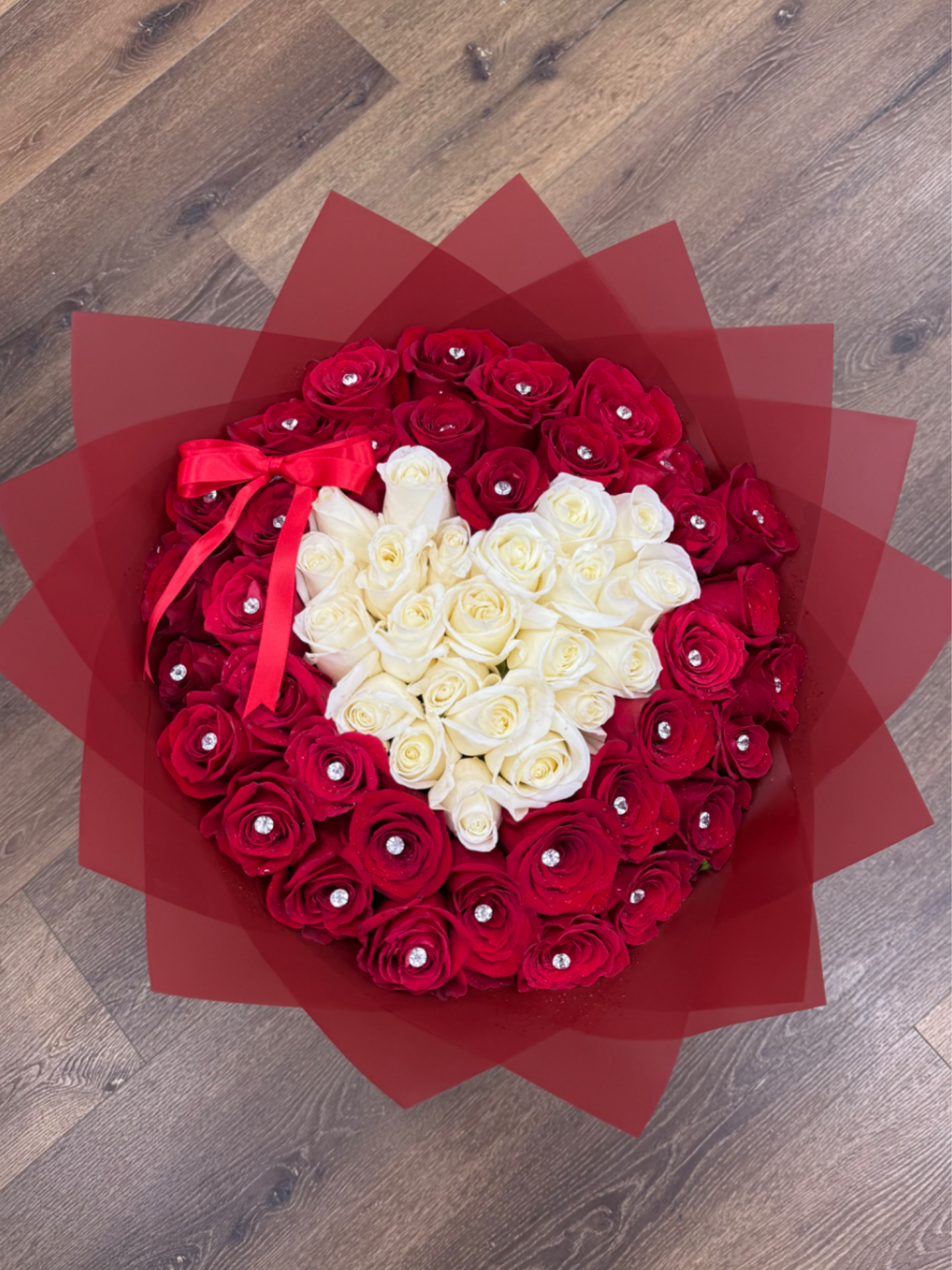 Round bouquet of red roses with a white heart of roses, wrapped in red paper with jewel accents