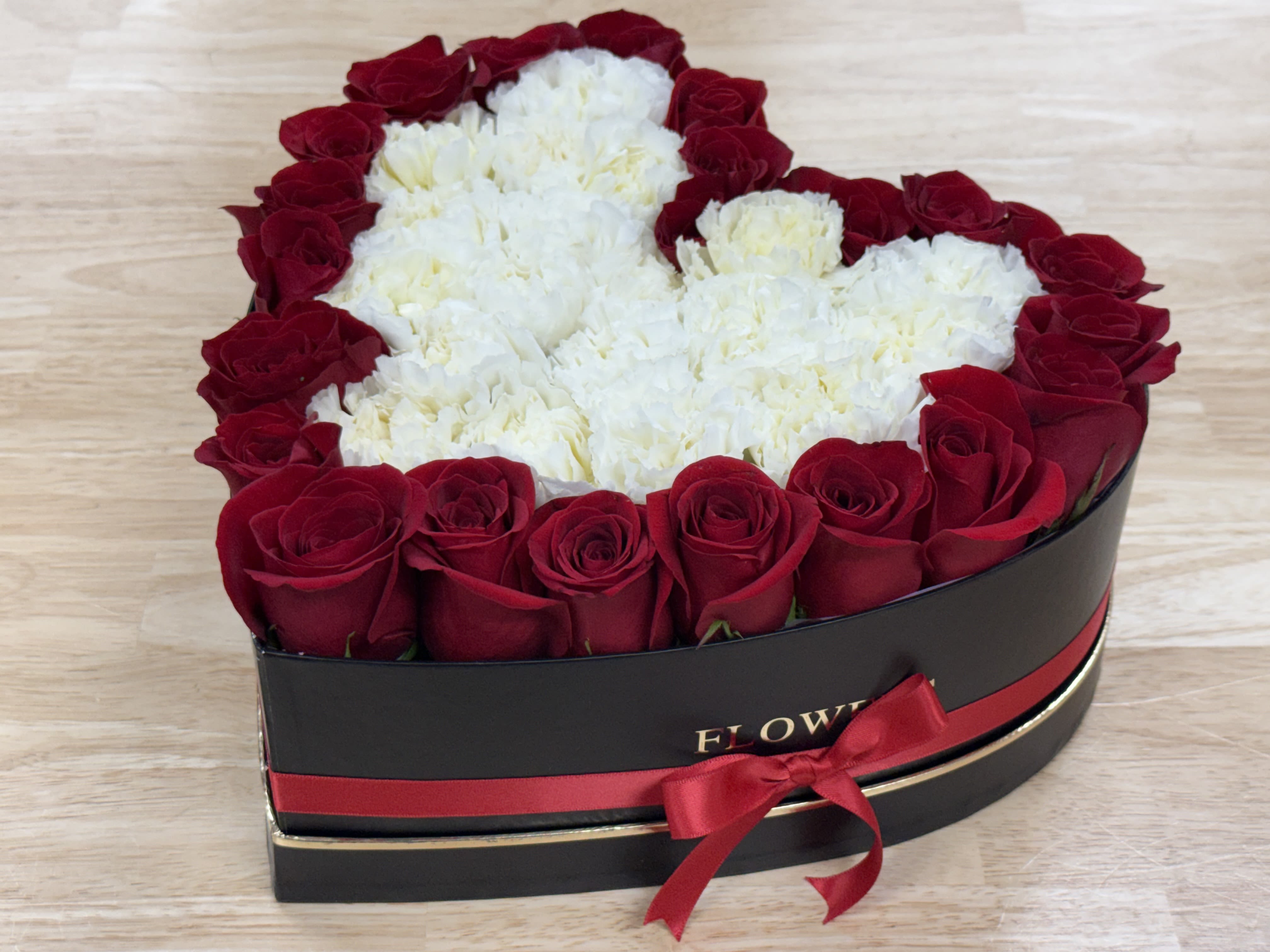 Heart-shaped box of red roses and white carnations with a red ribbon