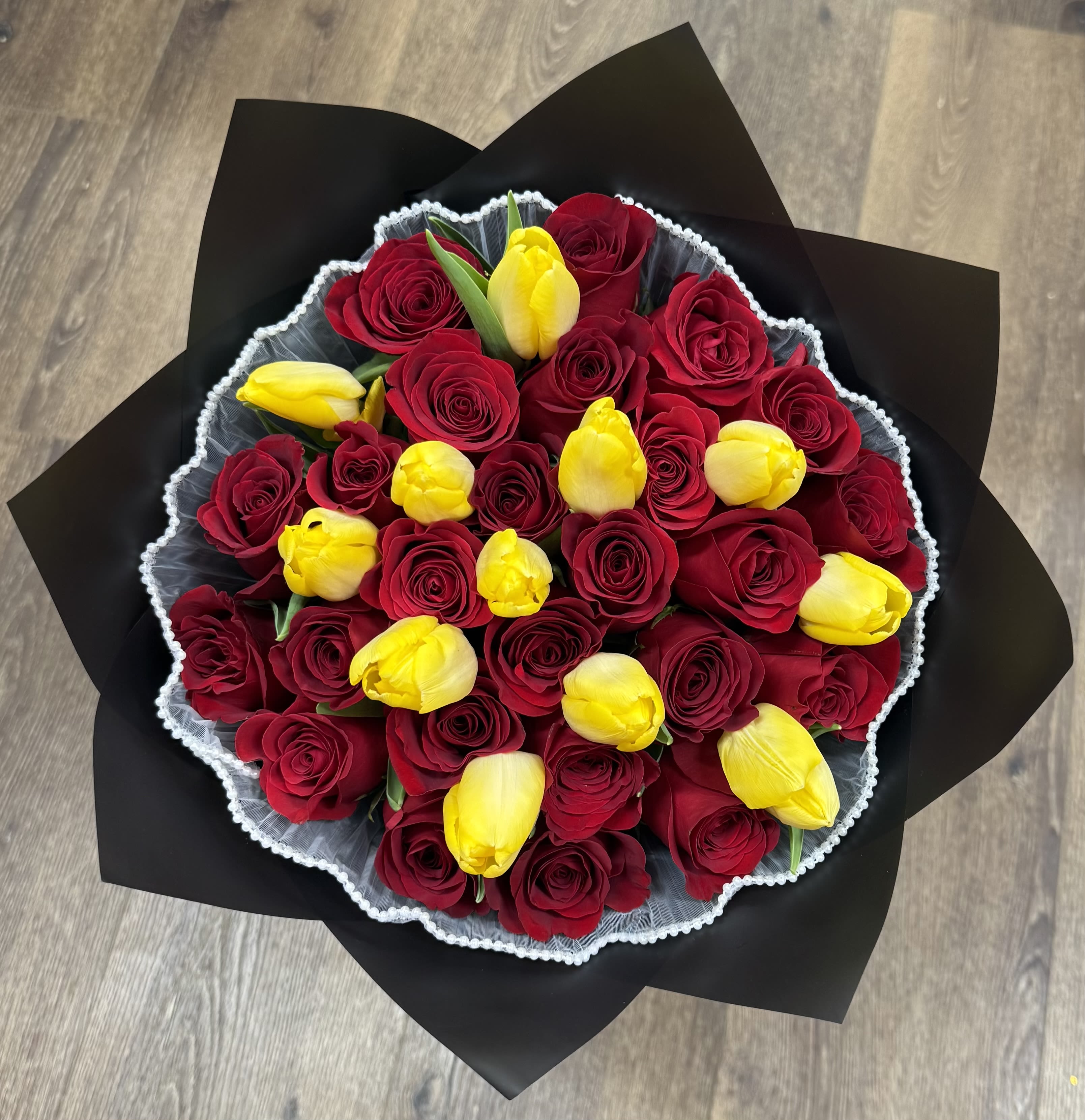 Bouquet of red roses and yellow tulips wrapped in black paper