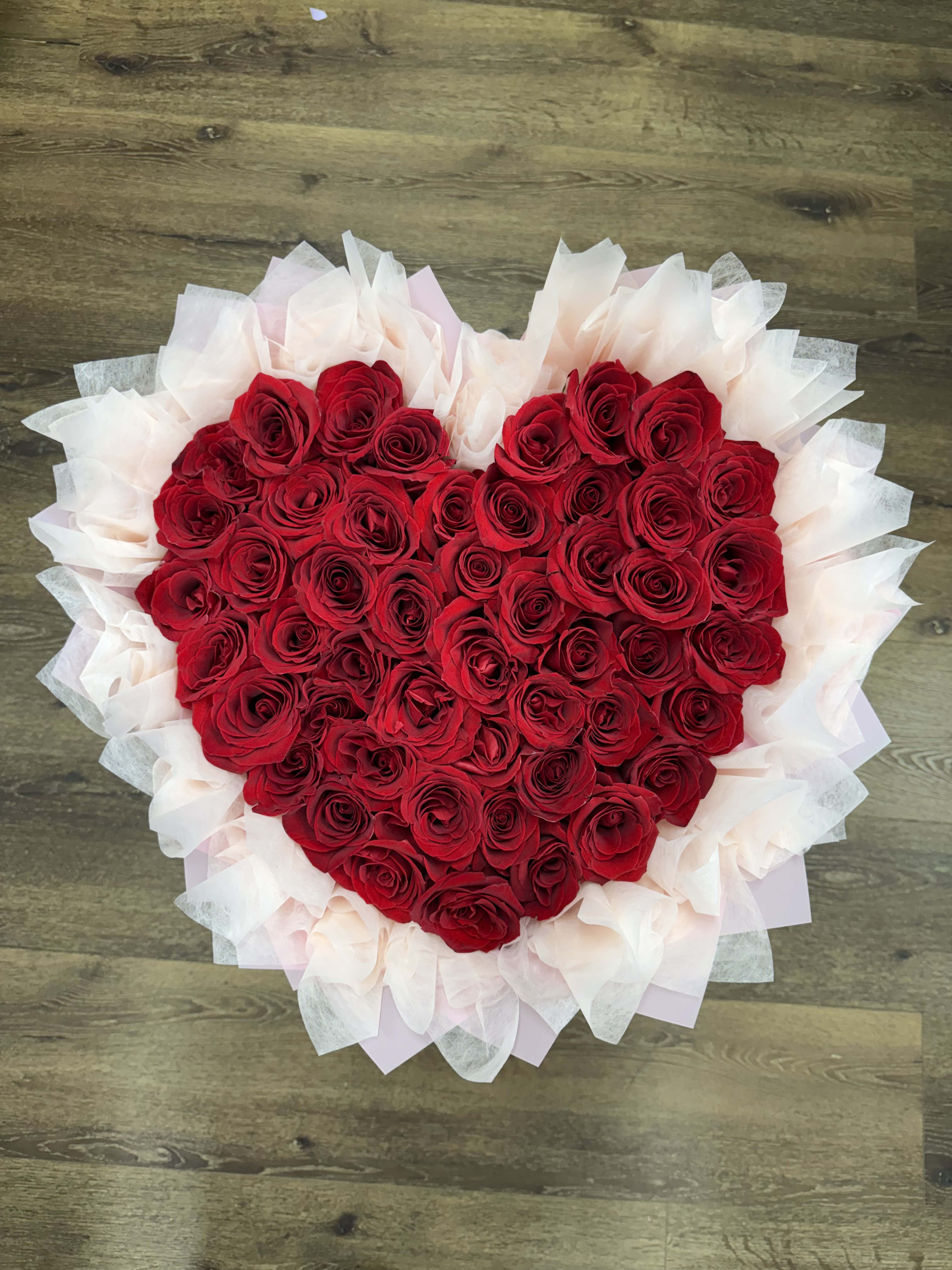 Heart-shaped bouquet of red roses wrapped in pale tissue paper