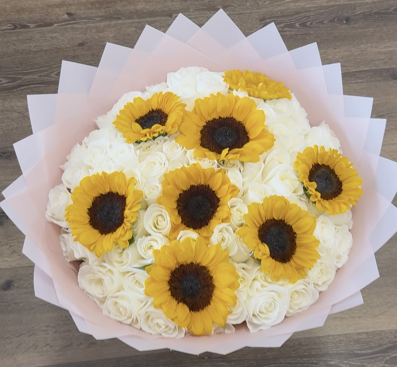 Sun-Kissed Cloud - The Sun-Kissed Cloud features a dense collection of white roses interspersed with several large sunflowers. This arrangement is finished in a layered pink Korean paper wrap.