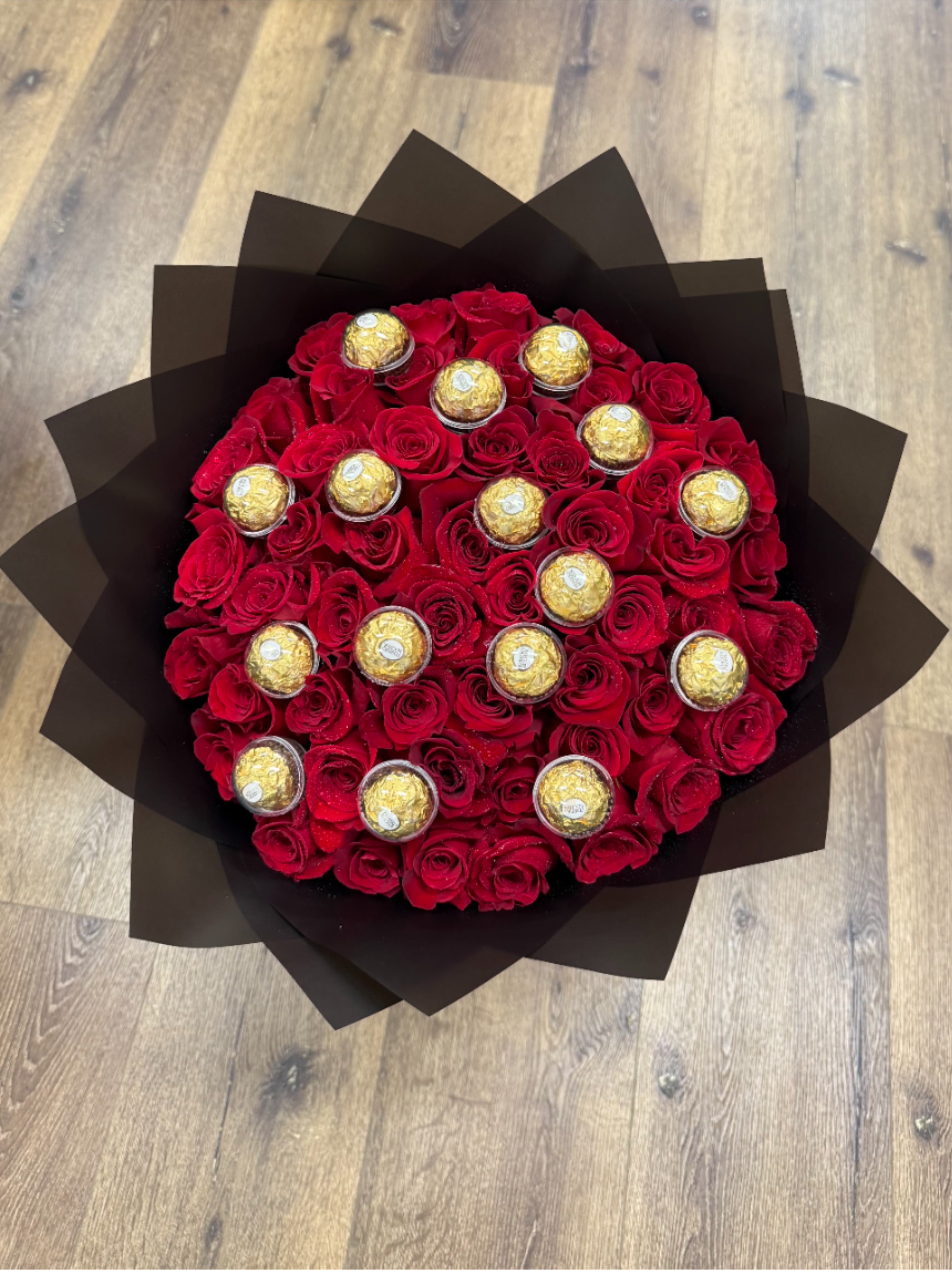 Round bouquet of red roses with gold-wrapped chocolates in black paper wrap