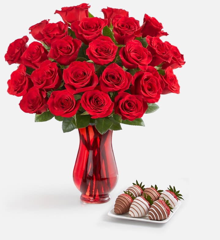 Red roses in a red glass vase with chocolate-covered strawberries on a tray