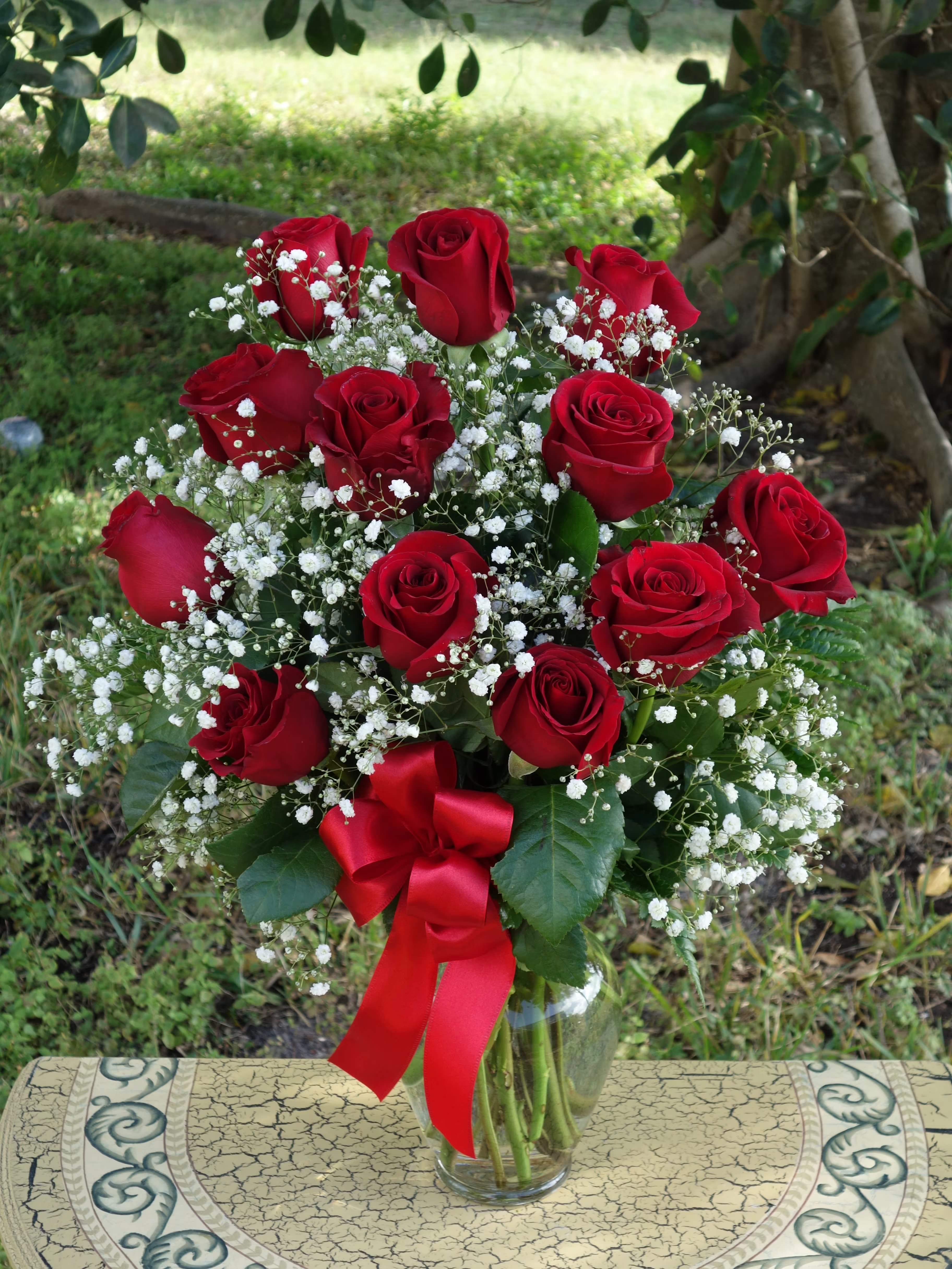 Red roses with baby's breath in a glass vase and red ribbon