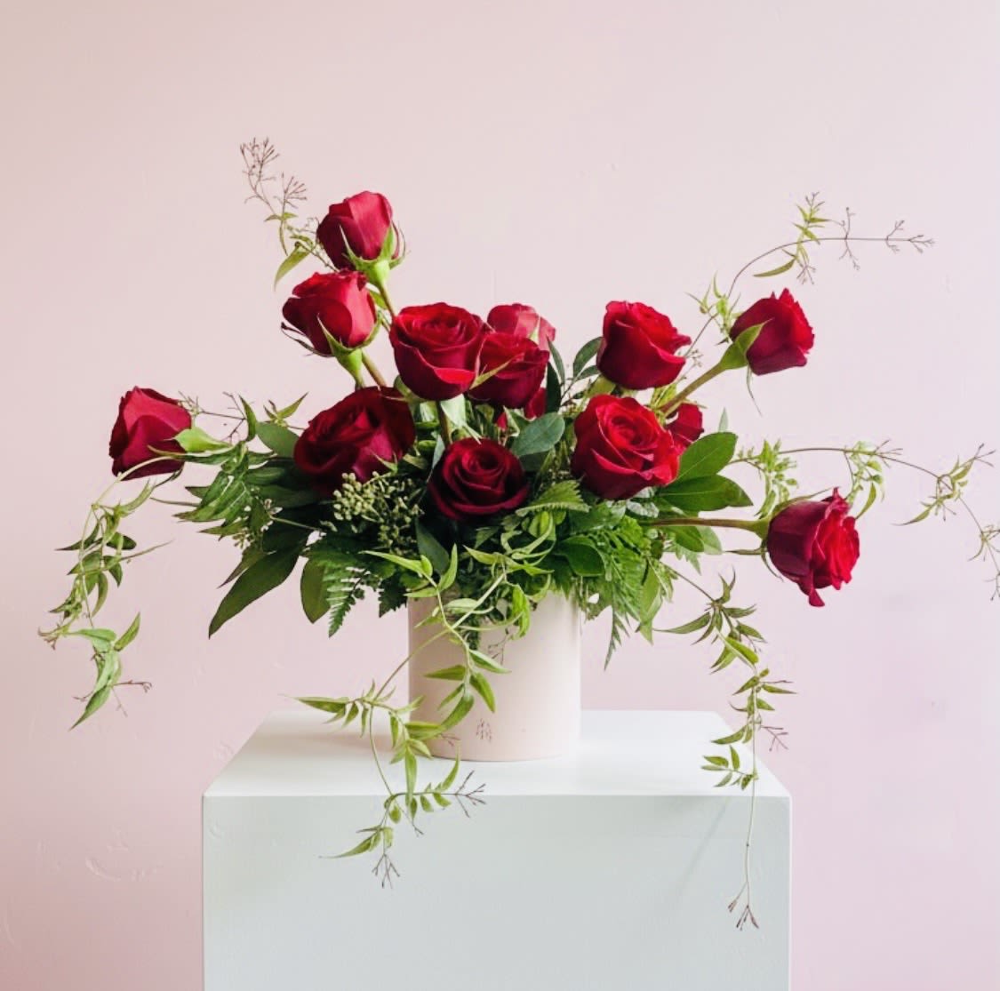 Red roses arranged in a white vase with trailing greenery
