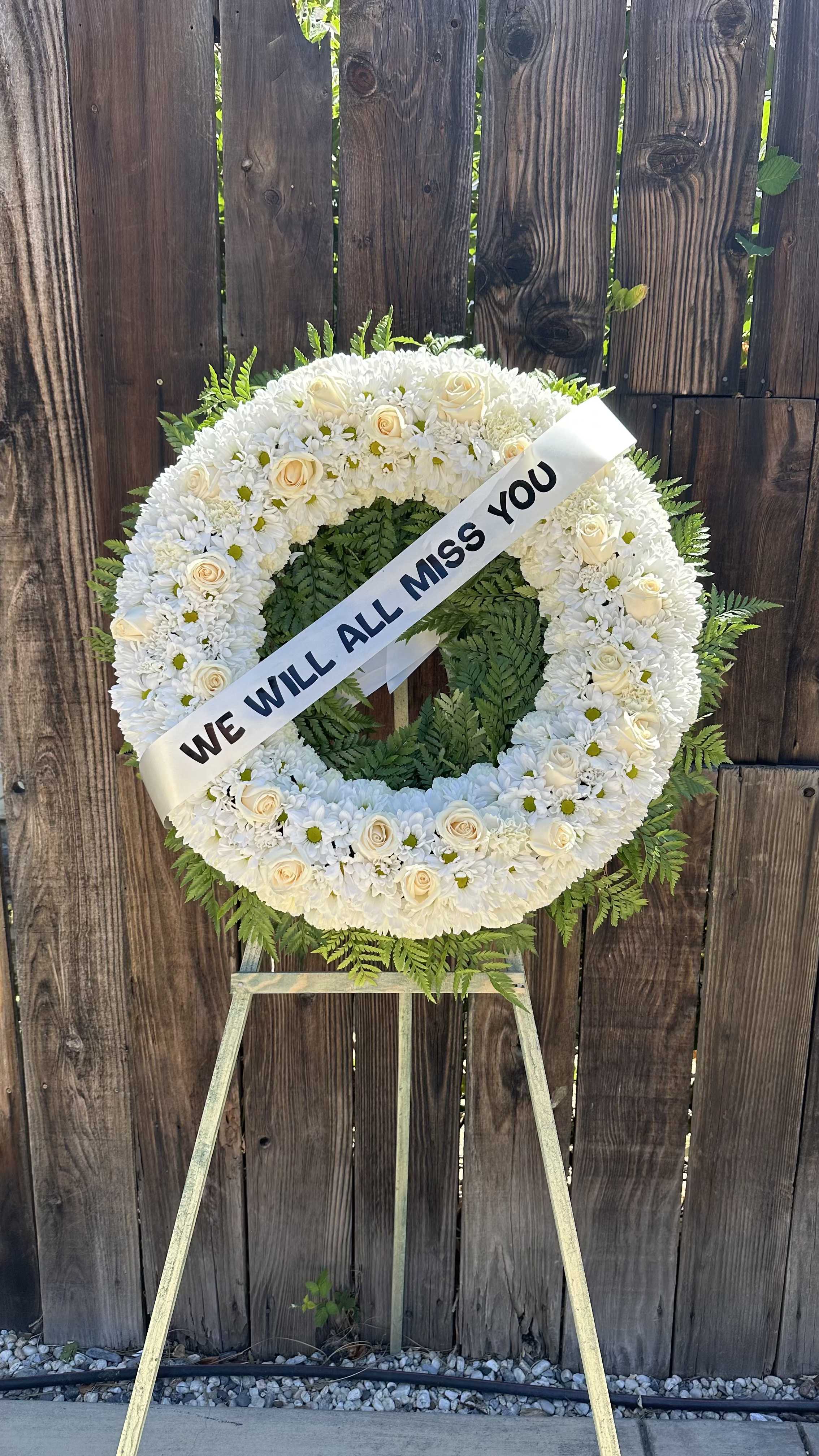 White funeral wreath on an easel with a memorial ribbon