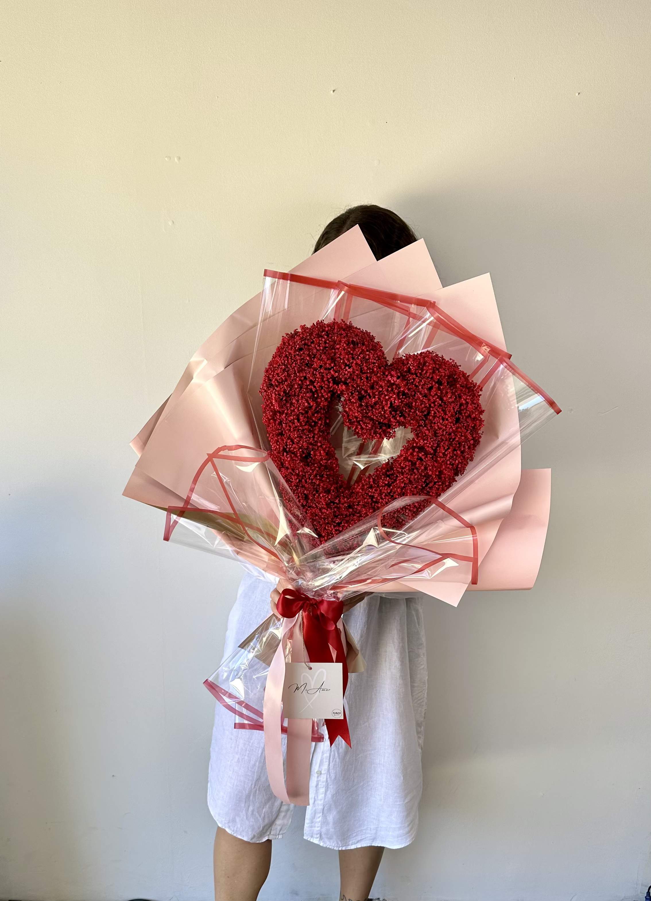 Heart-shaped red flower bouquet wrapped in pink paper and clear plastic