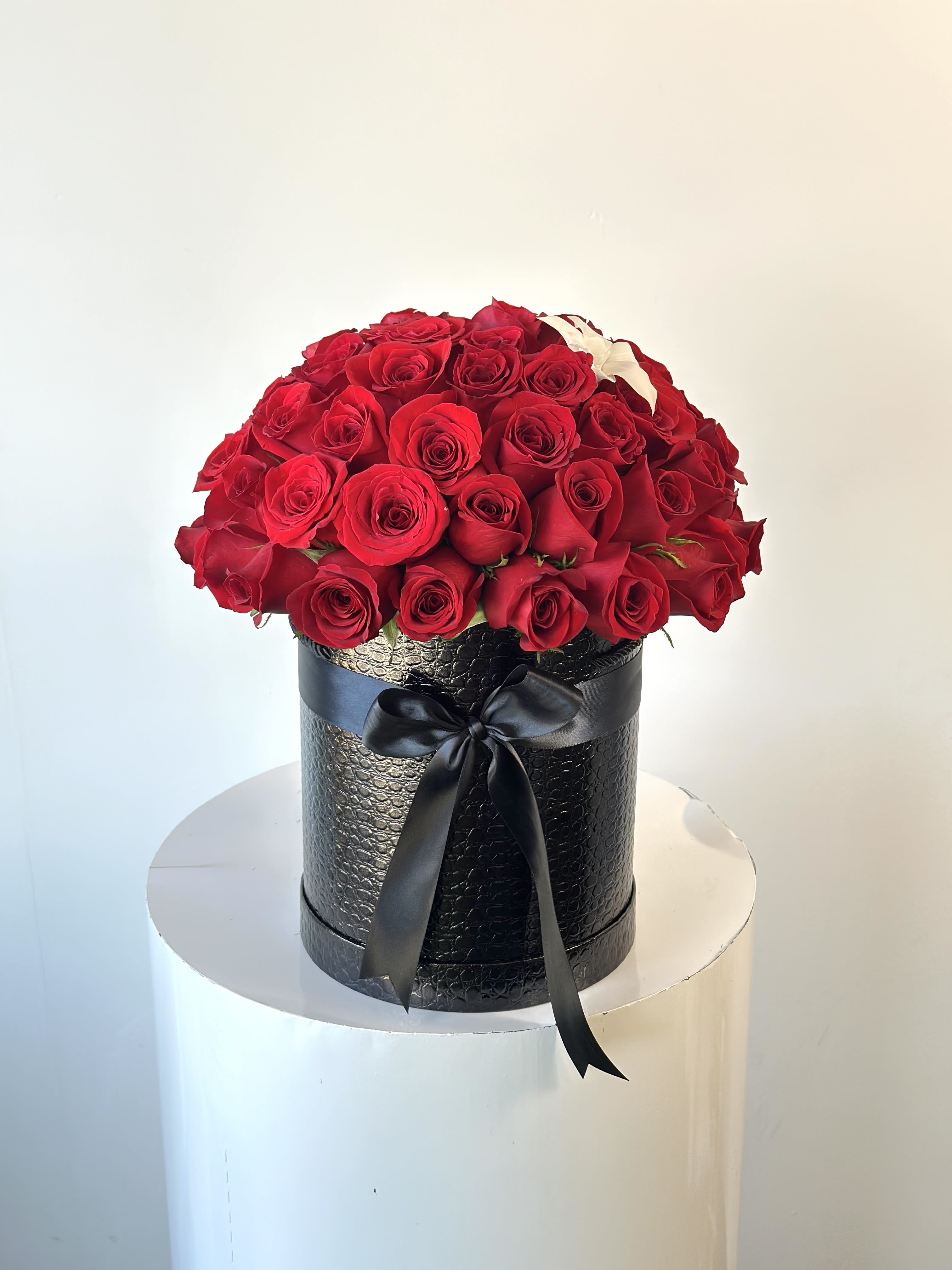 Red roses arranged in a black round box with a ribbon bow