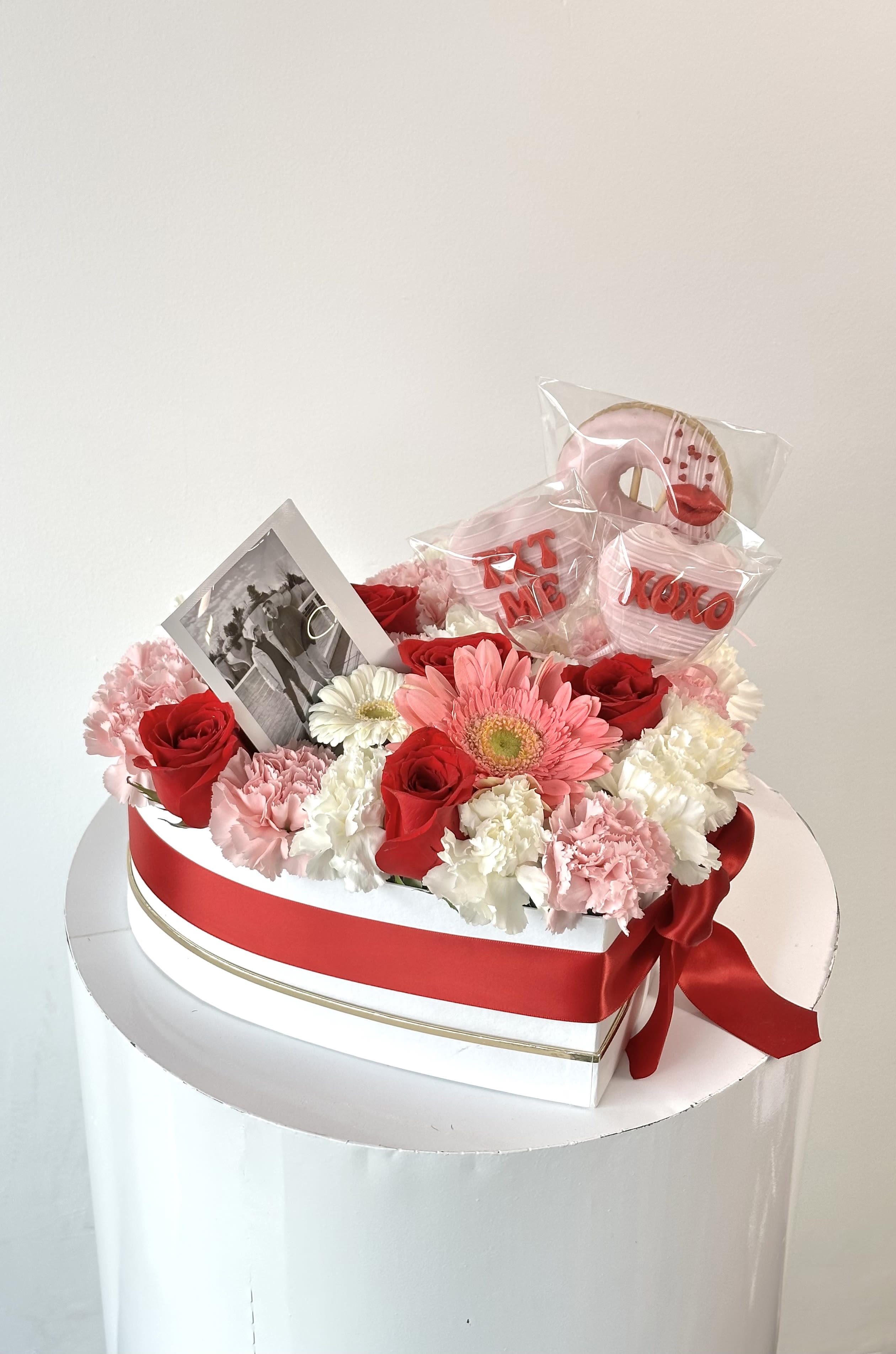 Heart-shaped flower box with red roses, pink and white carnations, and a photo card