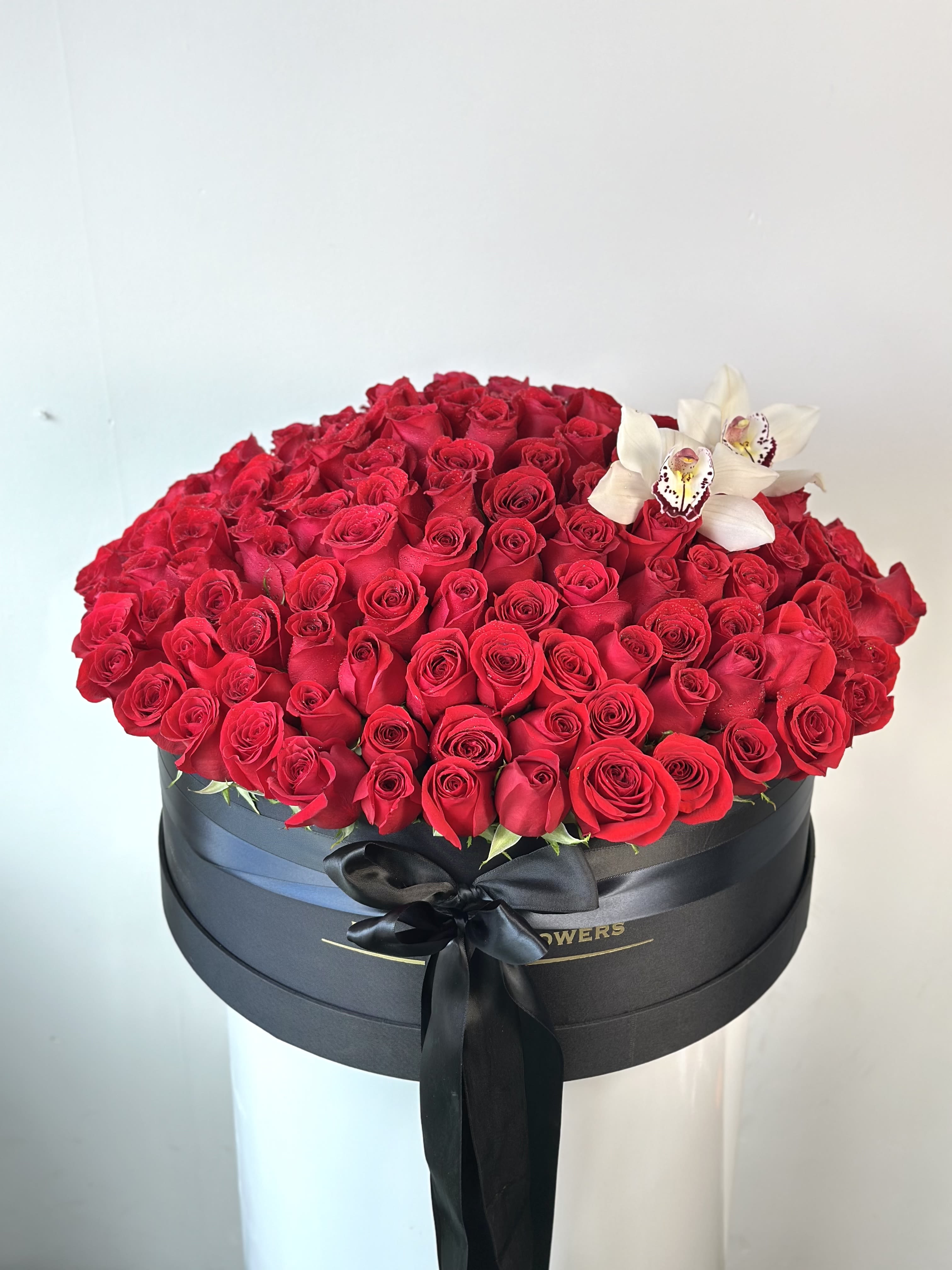 Large box of red roses with white orchids and a black ribbon