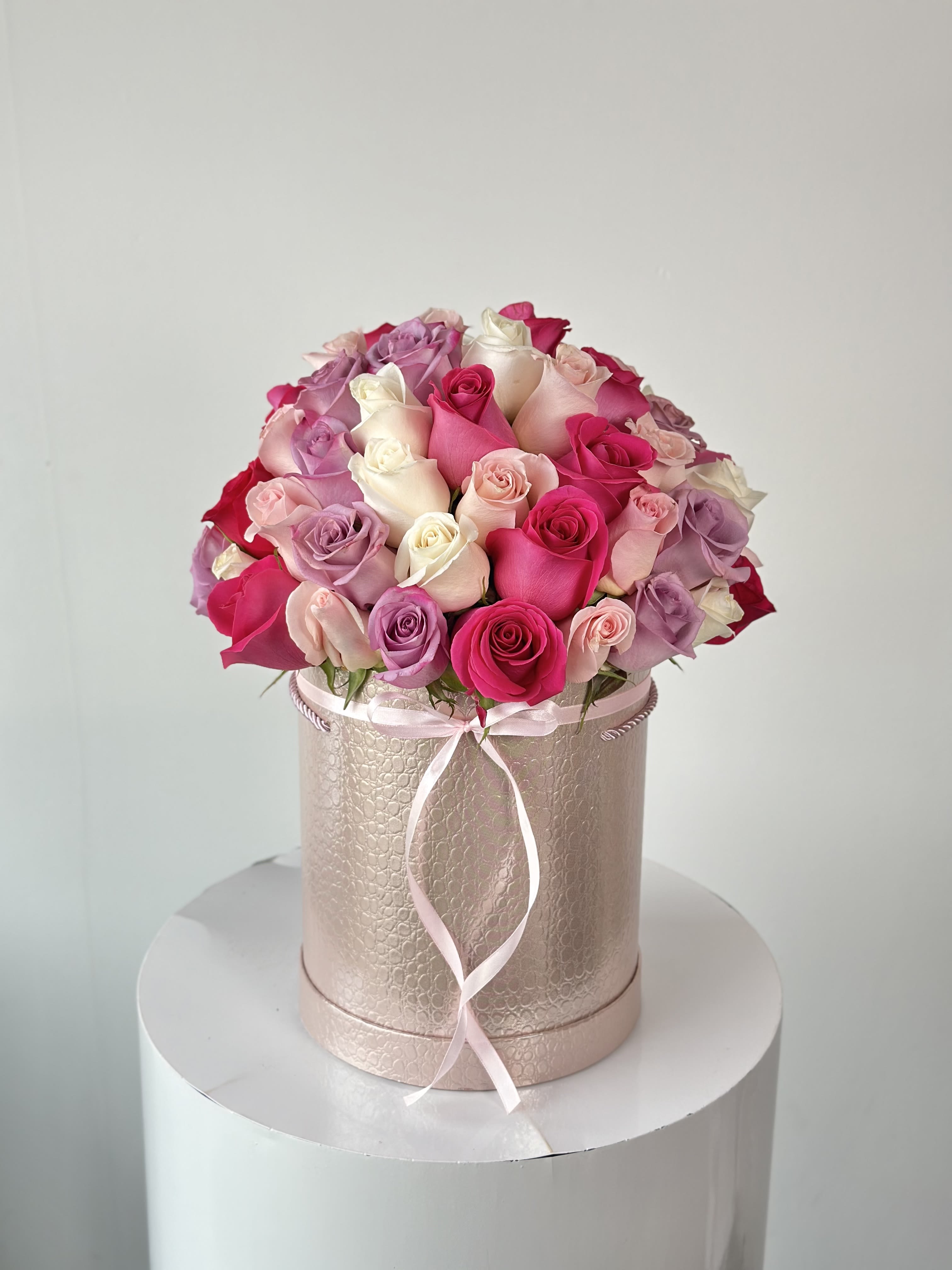 Pink and lavender roses arranged in a round hatbox with a ribbon