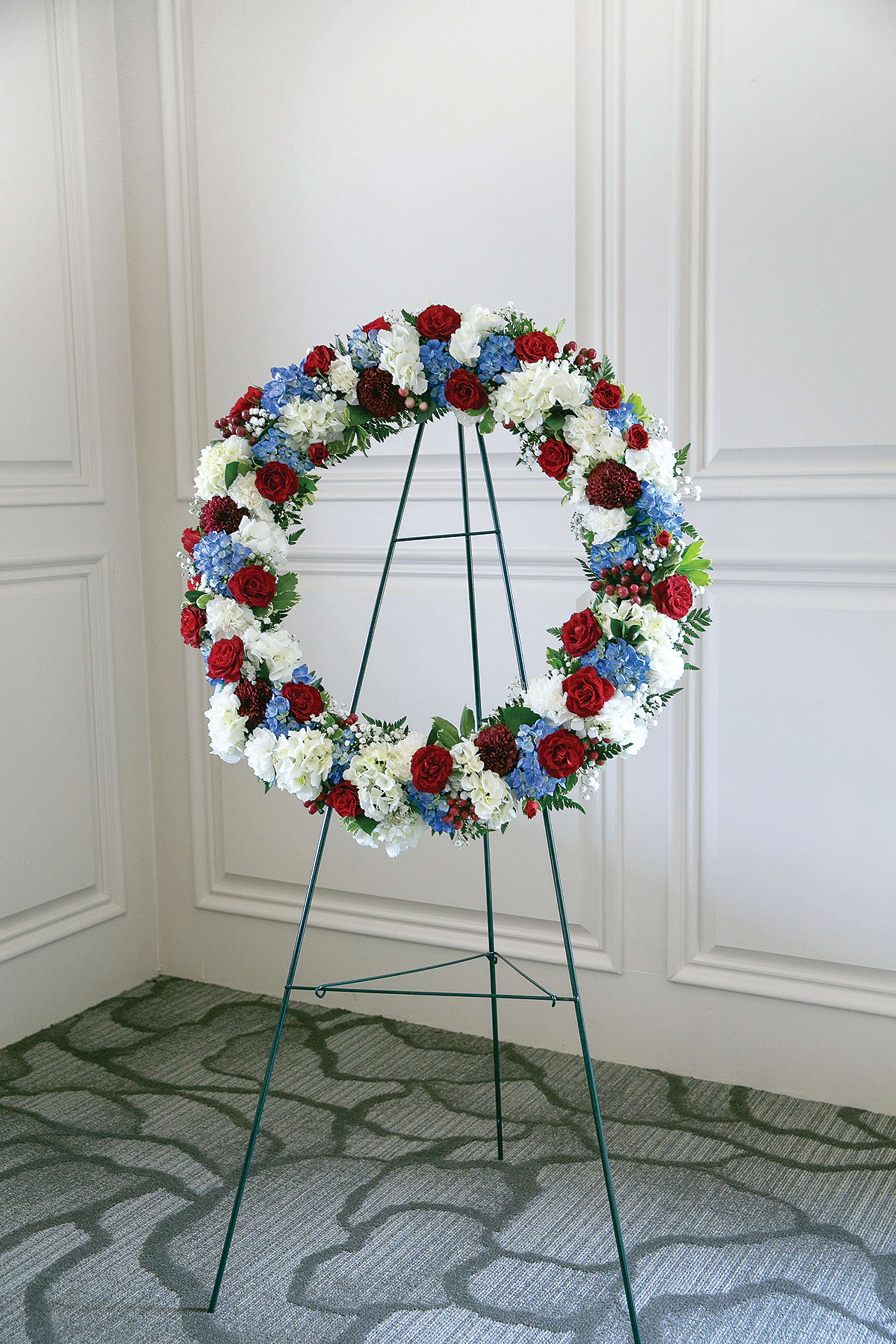 Circular floral wreath on a metal stand with red, white, and blue flowers