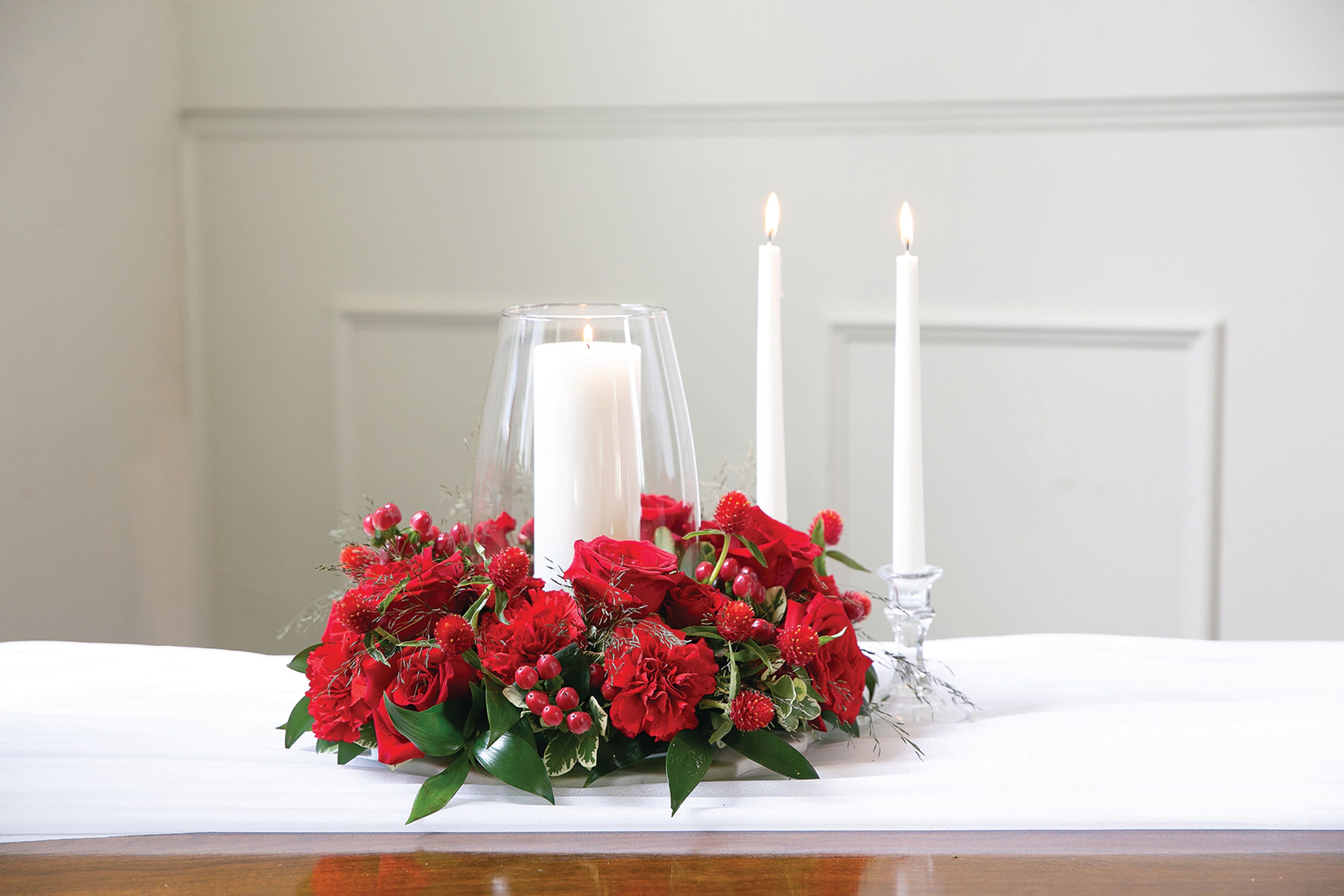 Red floral centerpiece with three white candles in glass holders
