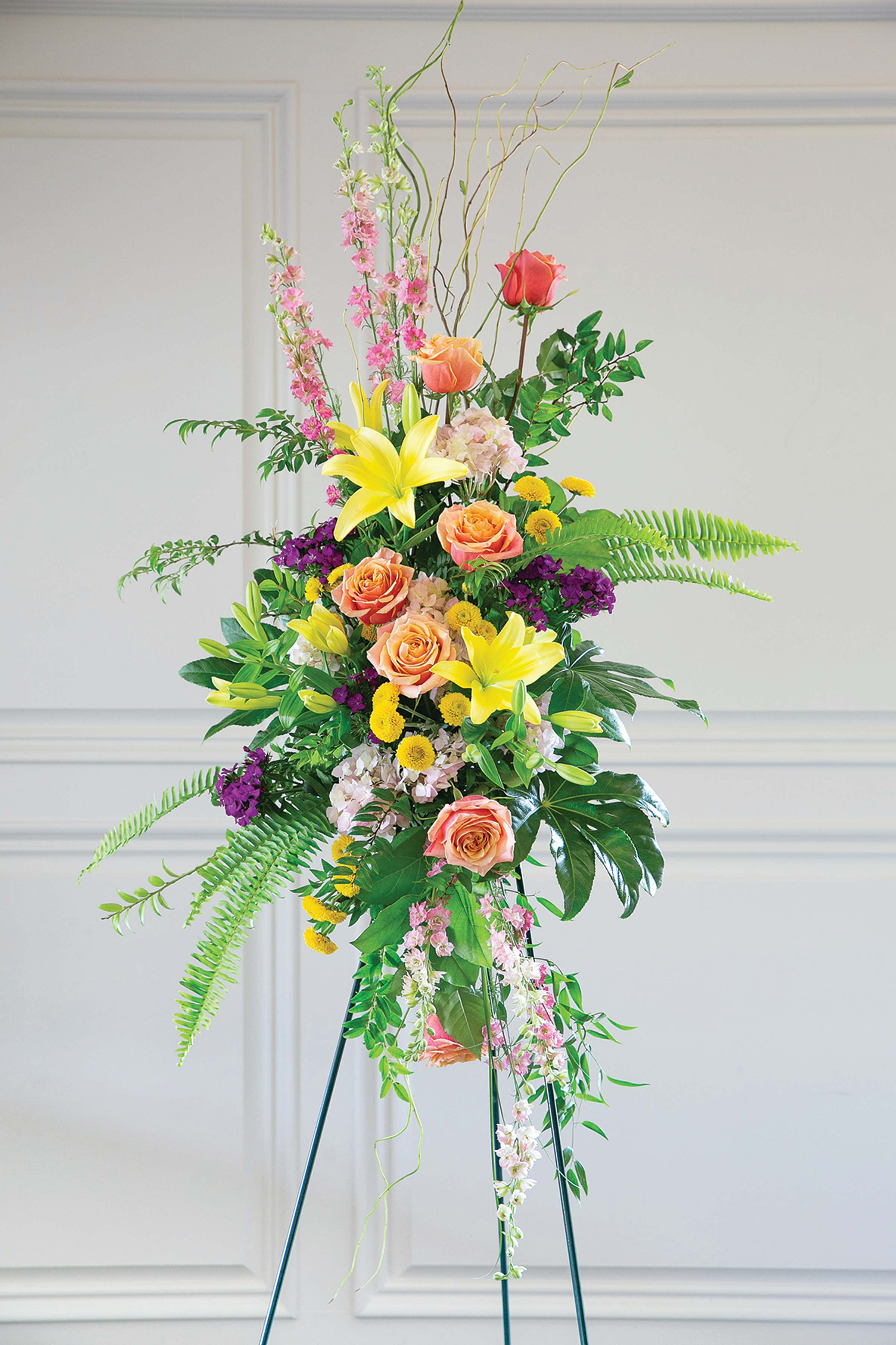 Tall floral standing arrangement with roses, lilies, and mixed blooms