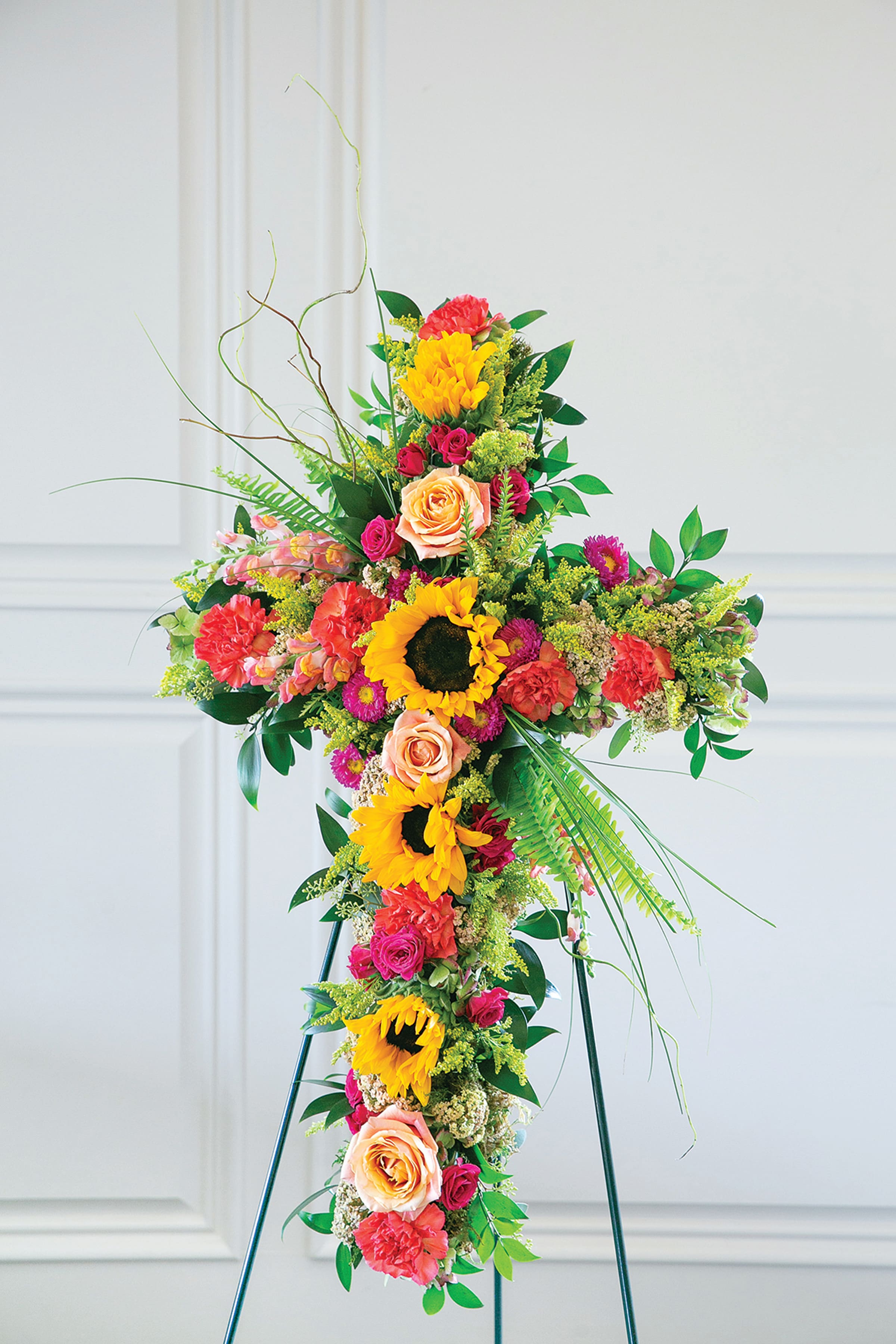 Tall floral cross on a stand with sunflowers, roses, and carnations