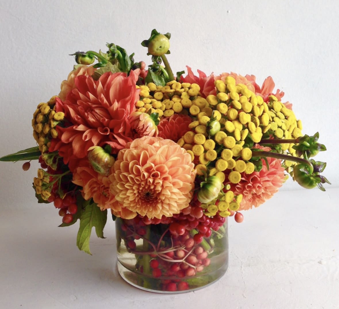 Low arrangement of orange dahlias and yellow button flowers in a clear glass vase