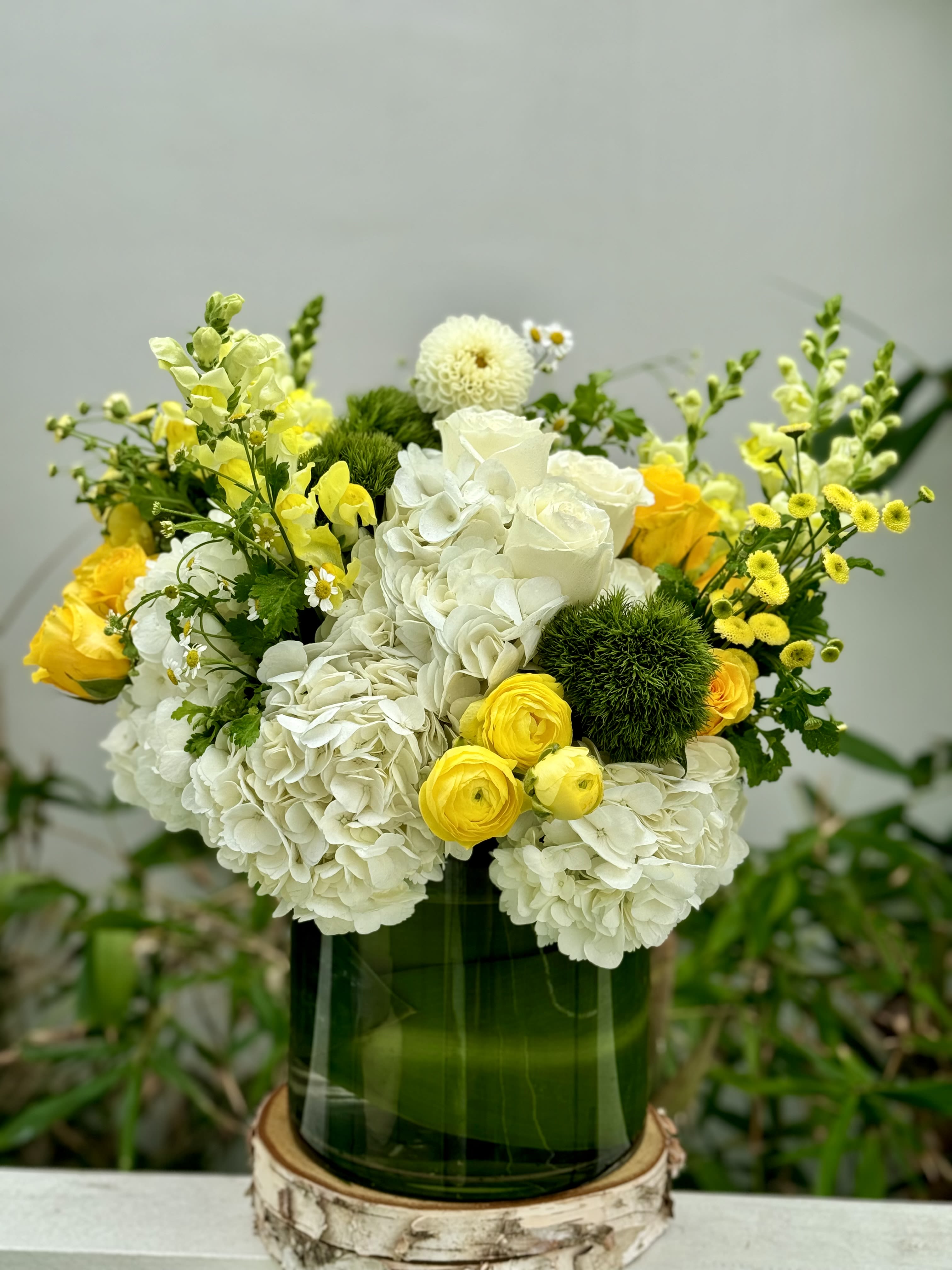 White and yellow flower arrangement in a green glass vase