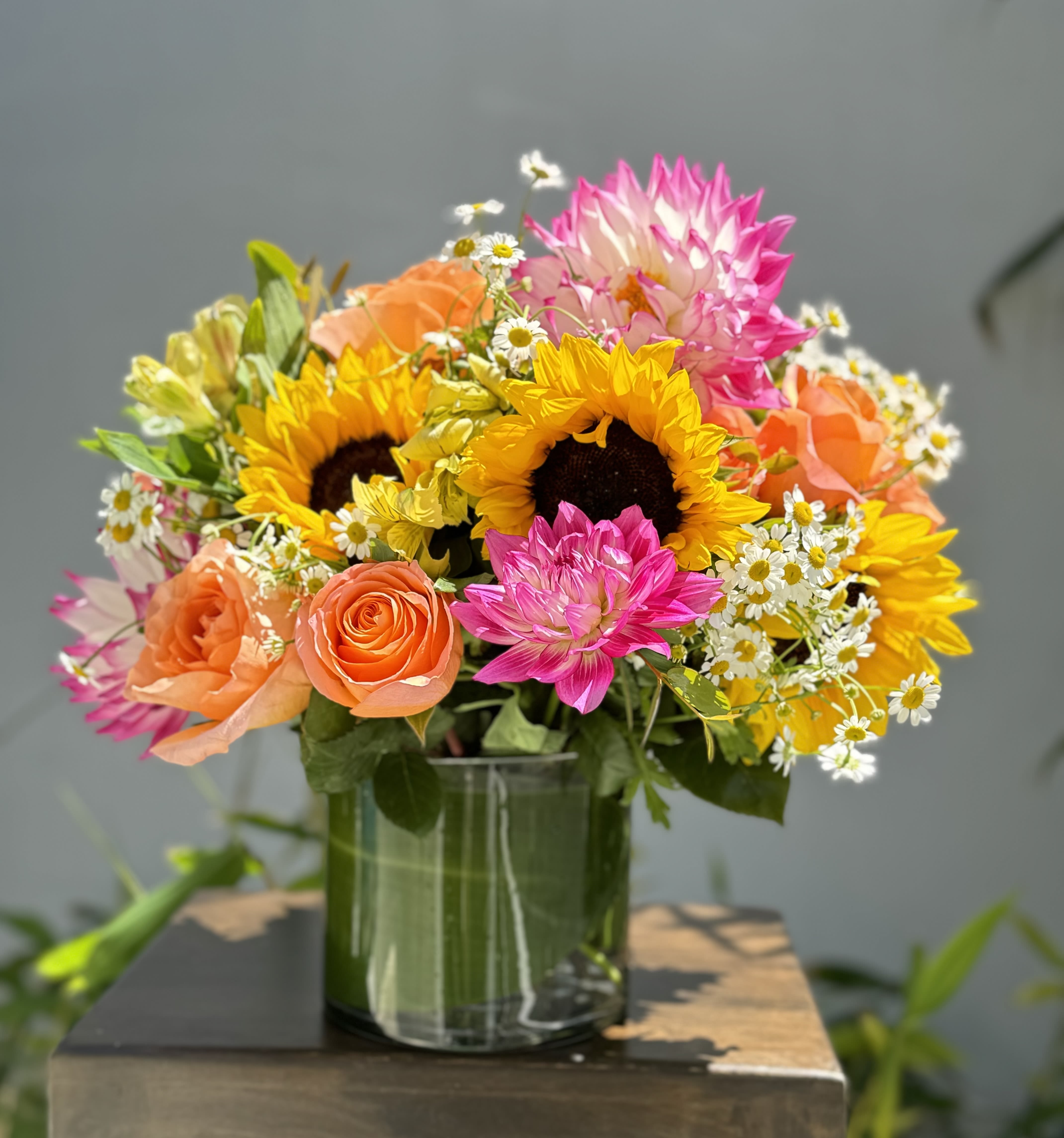 Bright mixed bouquet with sunflowers, roses, and daisies in a glass vase