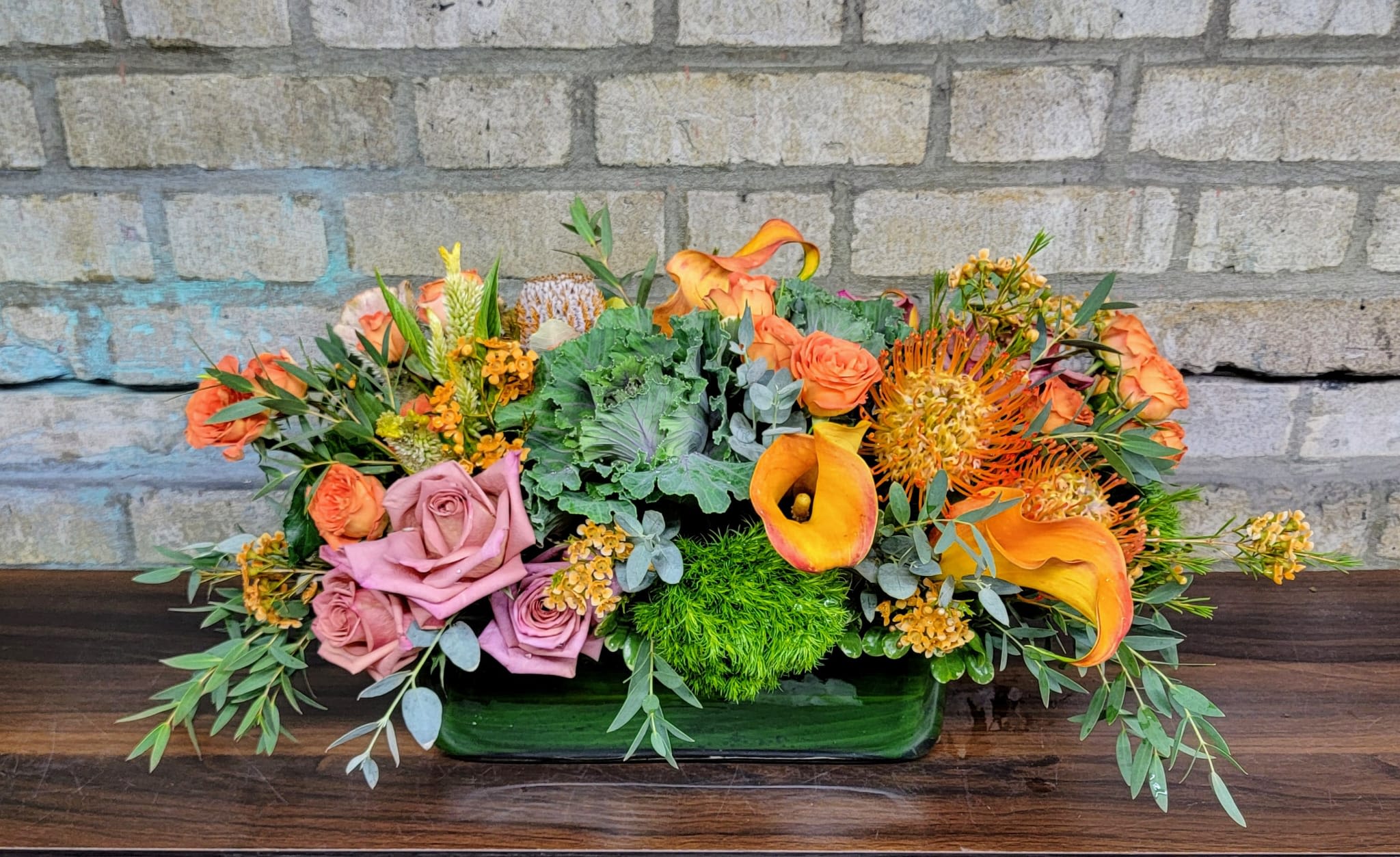 Orange and pink floral arrangement in a low green vase