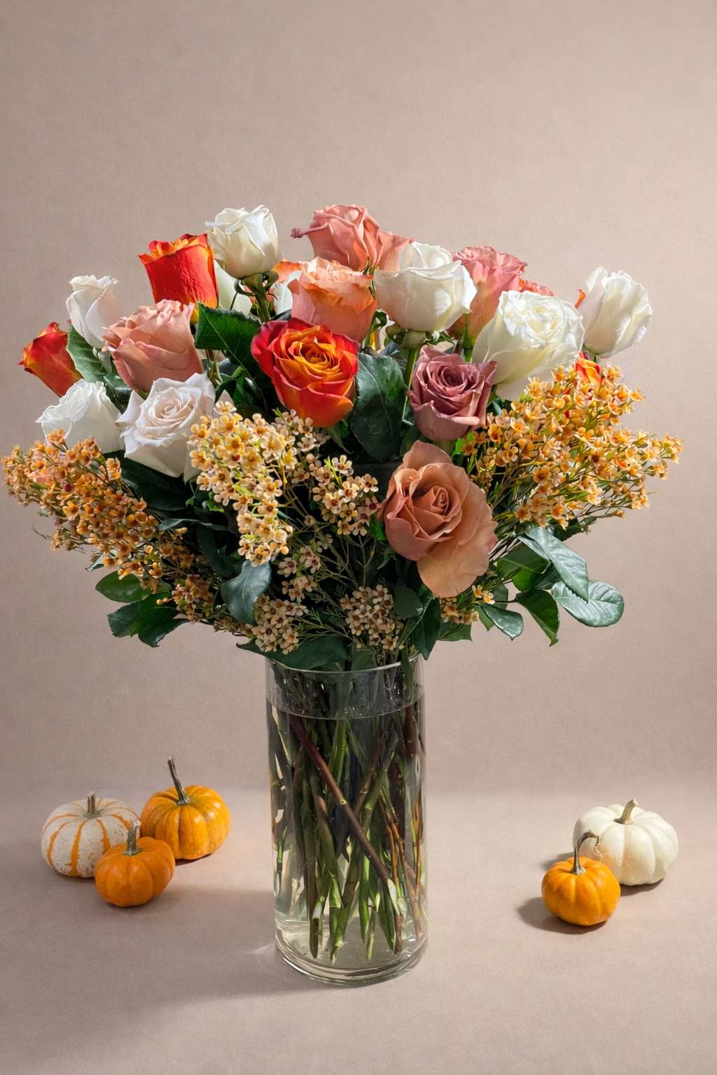 Mixed roses in a clear glass vase with small pumpkins around it