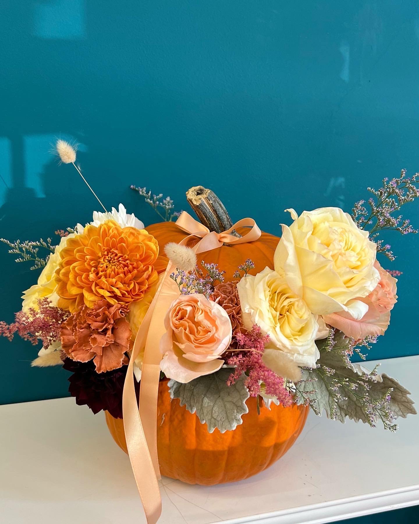 Floral arrangement in a pumpkin with orange, cream, and peach blooms