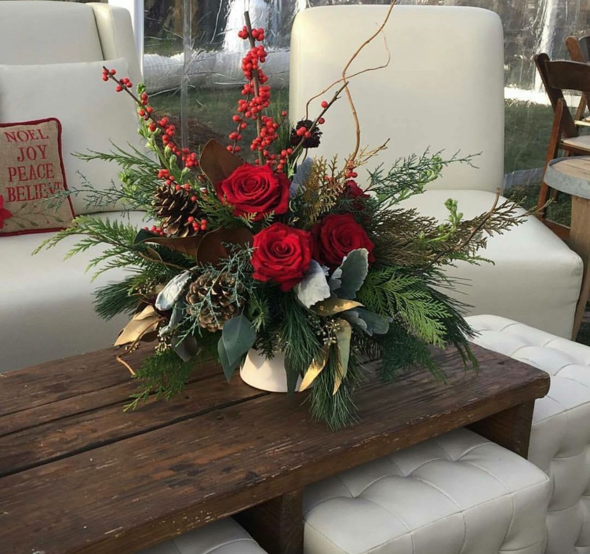 Red roses and berries in a white vase with pinecones and evergreen branches