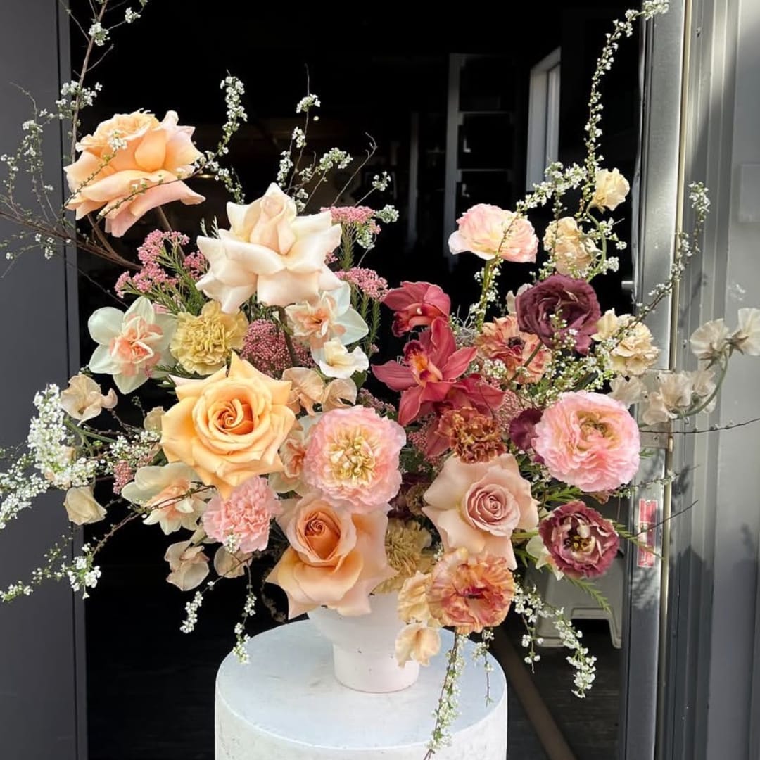Large floral arrangement with peach, pink, and burgundy blooms in a white vase