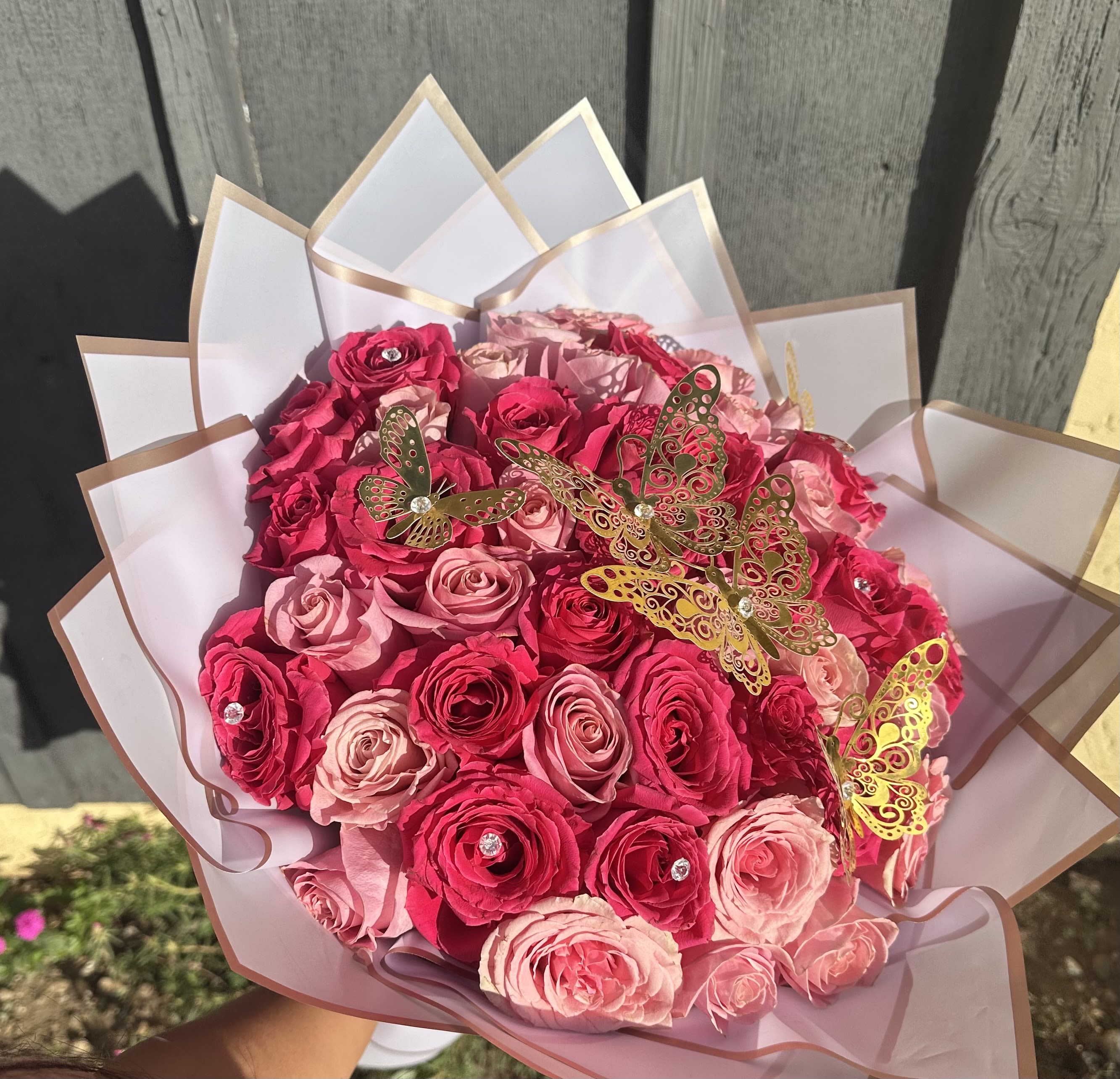 Bouquet of pink and hot pink roses wrapped in white paper with butterfly decorations