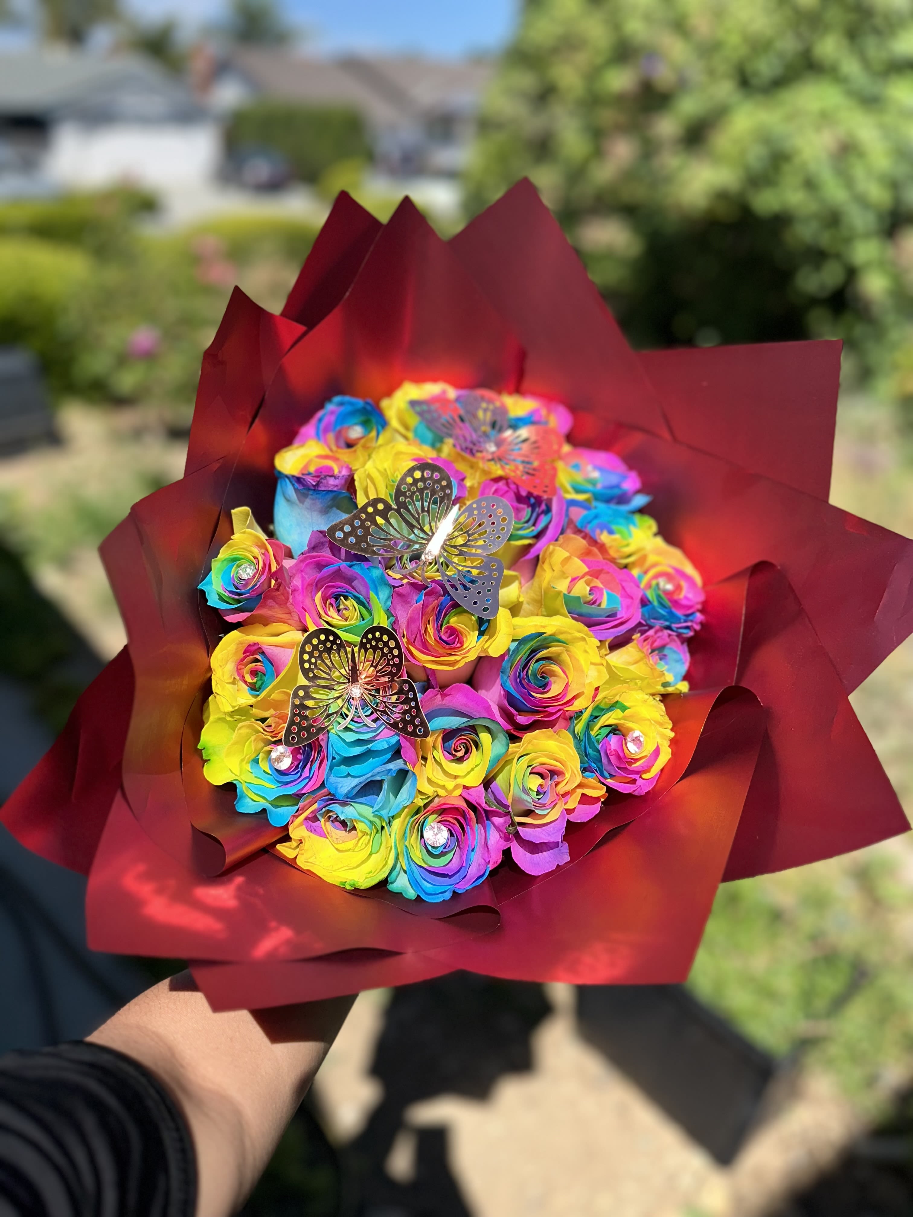 Rainbow bouquet of roses wrapped in burgundy paper with butterfly picks