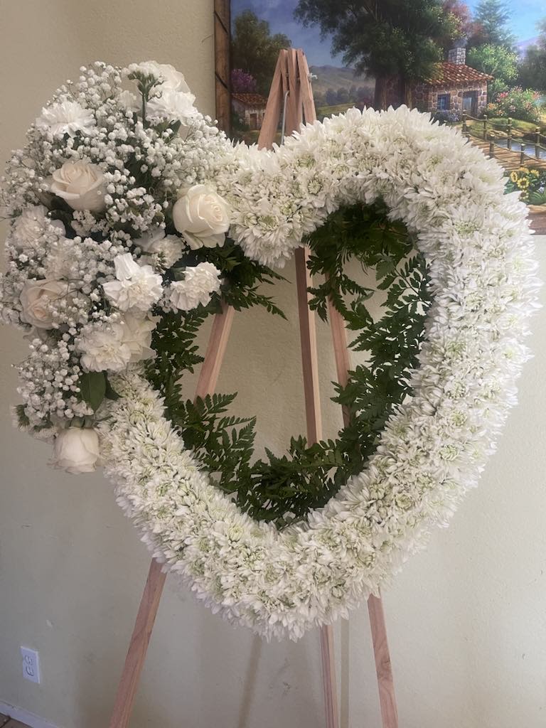 White floral heart wreath on a wooden easel with roses and chrysanthemums
