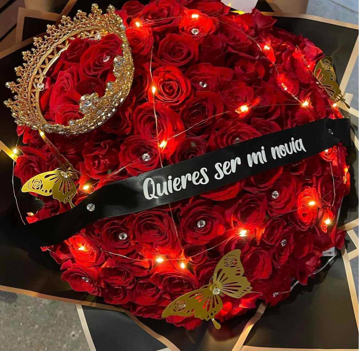 Red rose bouquet with a jeweled crown and a black ribbon reading "Quieres ser mi novia"