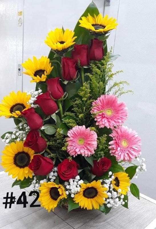 Tall floral arrangement with sunflowers, red roses, and pink gerbera daisies