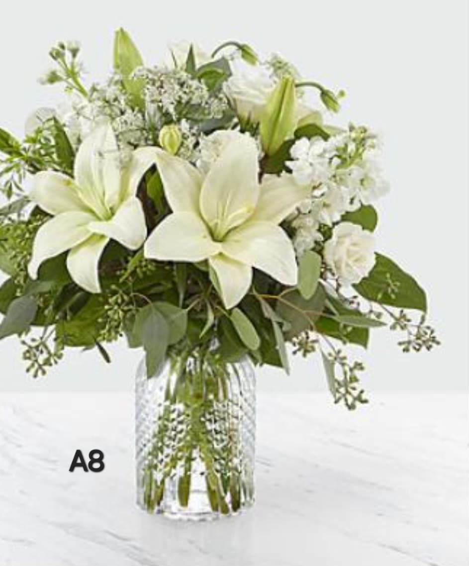 White lilies and mixed white flowers in a clear glass vase