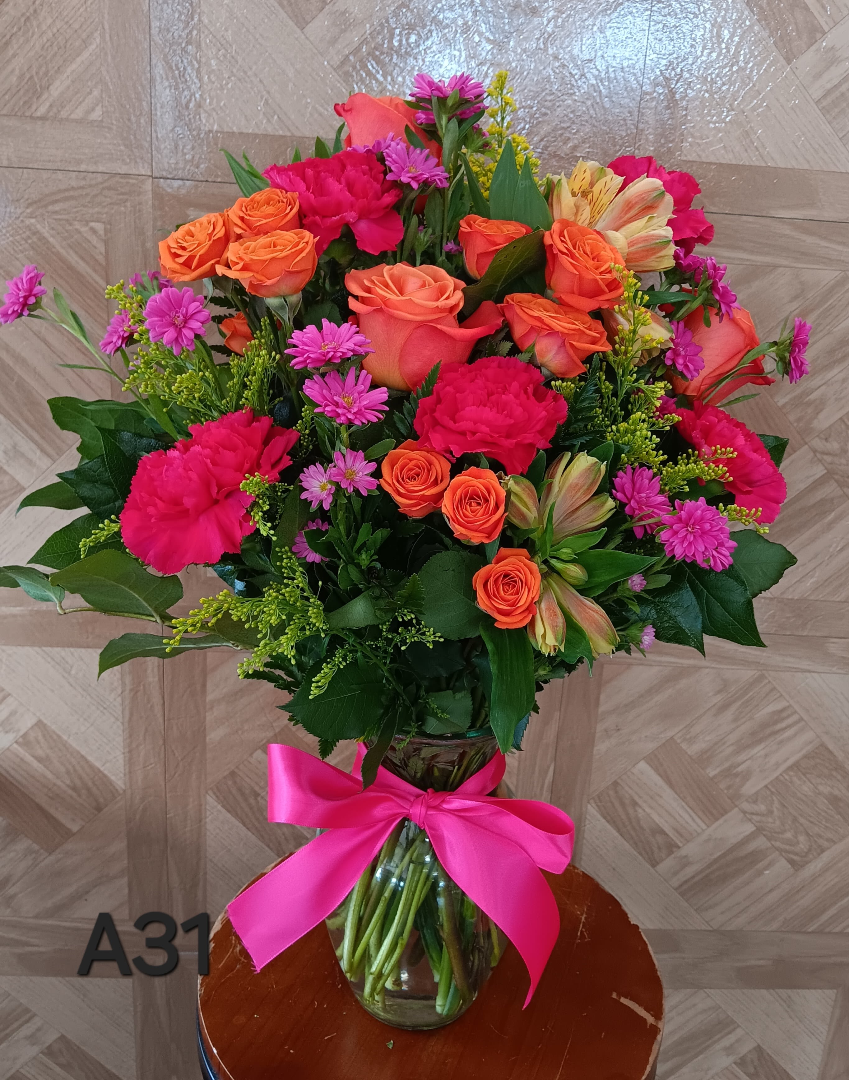 Tall vase arrangement of bright orange roses and hot pink flowers with a pink bow.