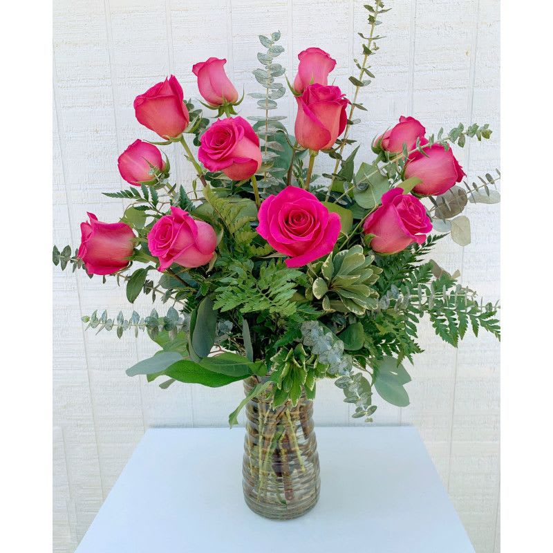 Pink roses arranged in a clear glass vase with eucalyptus and fern foliage.
