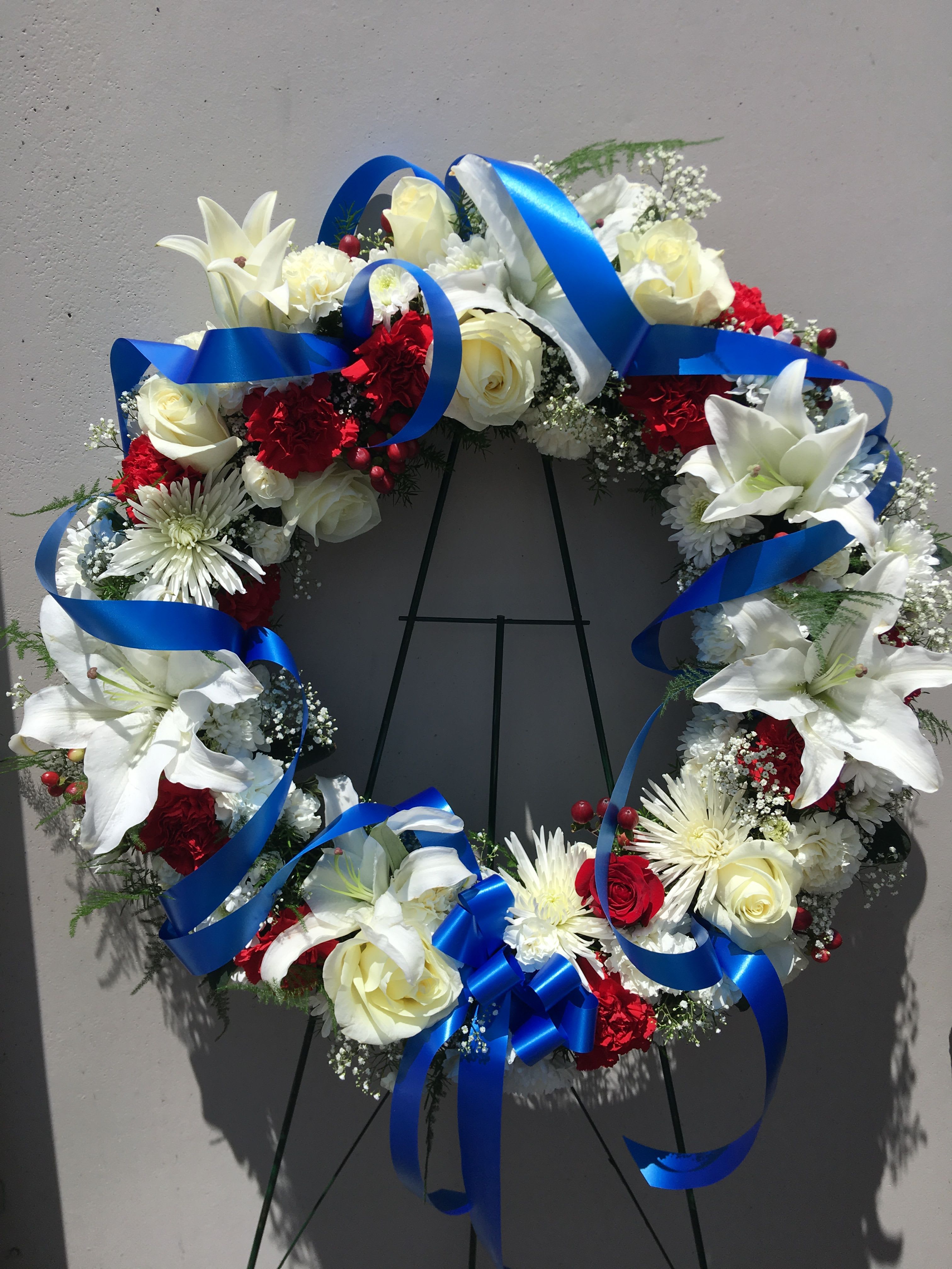 Circular wreath of white lilies, roses, and red carnations with blue ribbon