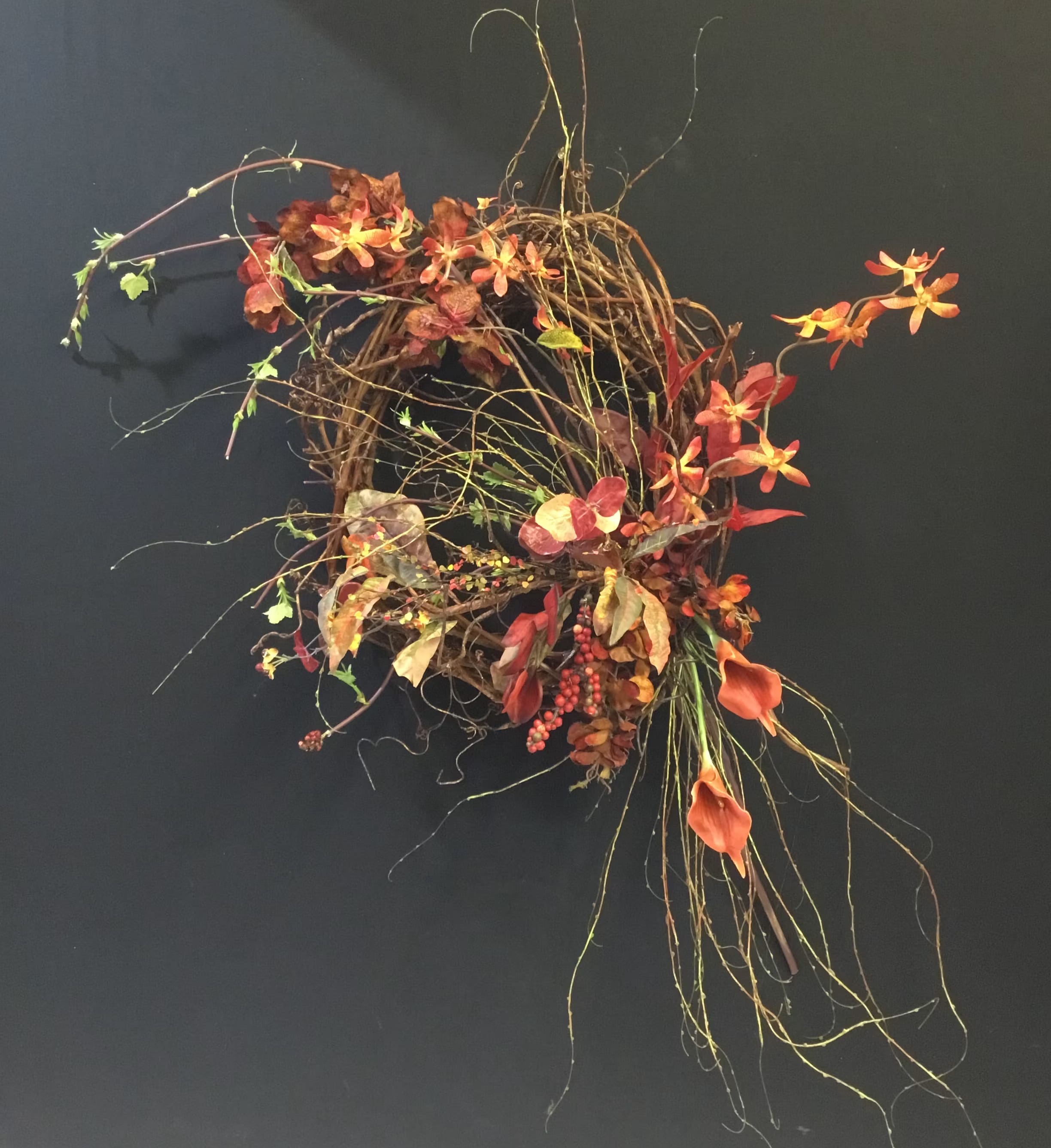 Abstract floral wreath with orange blooms and trailing vines on a dark background
