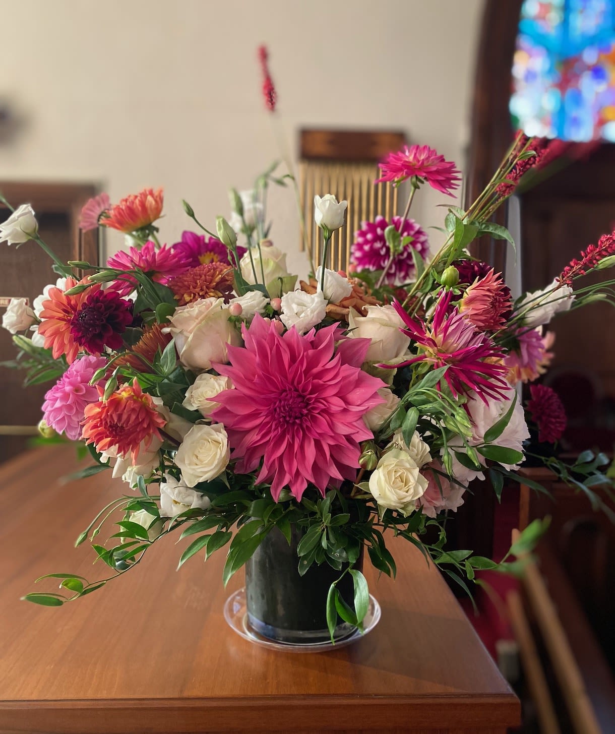 Low glass vase of pink dahlias and white roses with mixed bright blooms on a wooden table