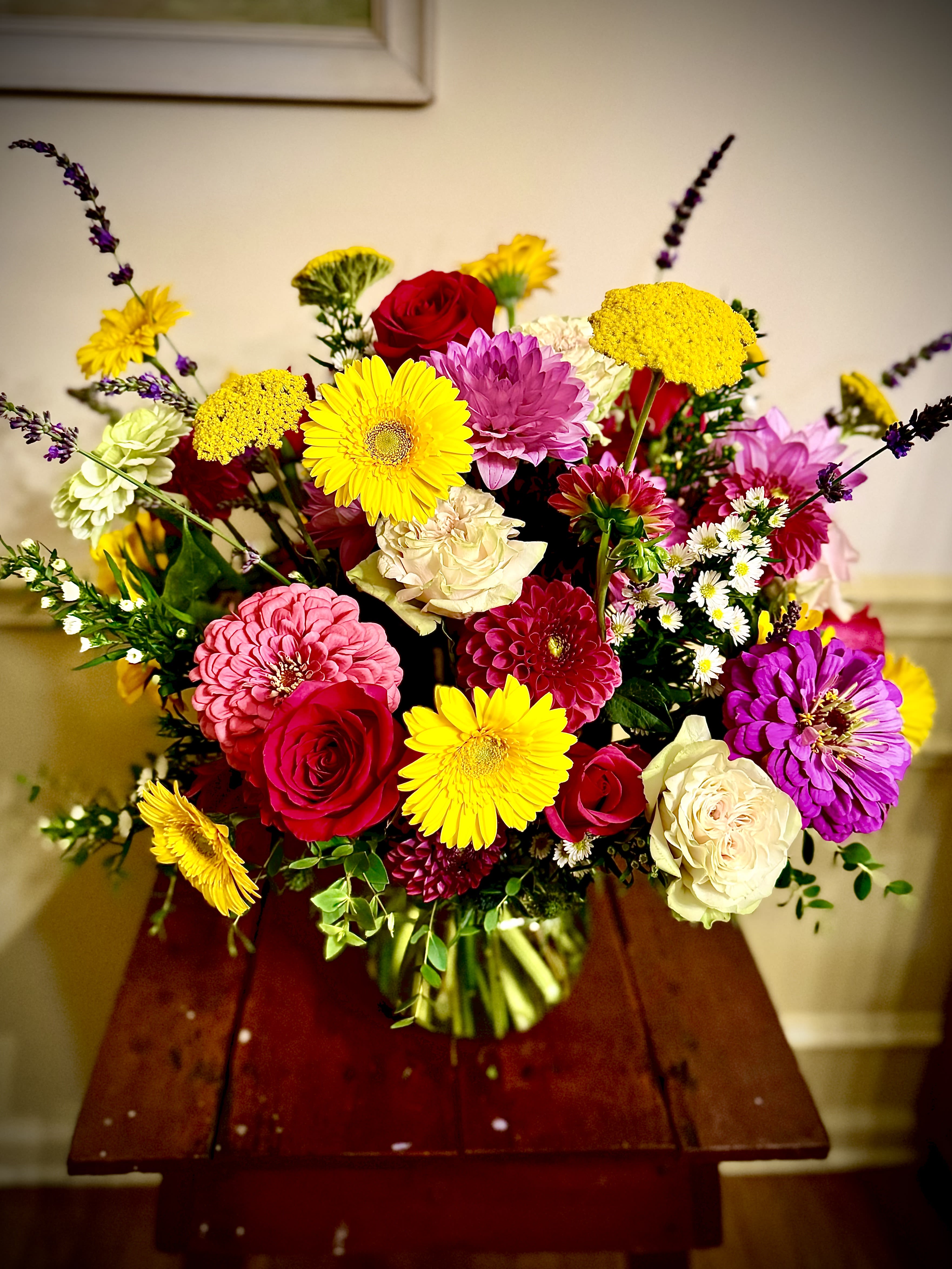 Bright mixed bouquet of yellow gerbera daisies, red roses, and assorted blooms in a clear glass vase