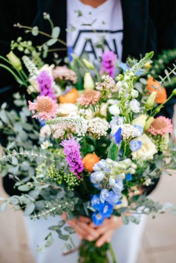 Loose hand-tied bouquet of colorful mixed flowers in purple, blue, white, and orange tones