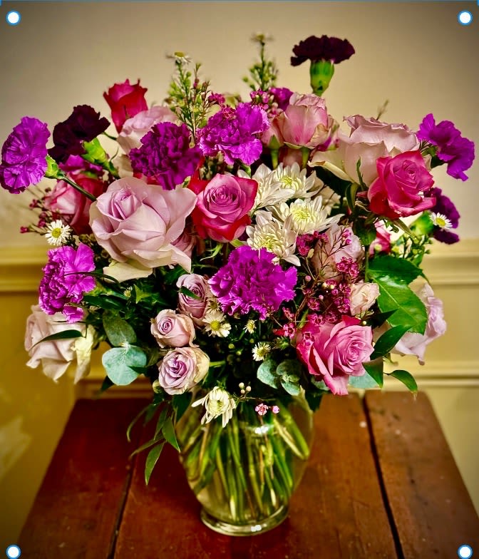 Mixed bouquet of pink and purple roses, carnations, and white daisies in a clear glass vase