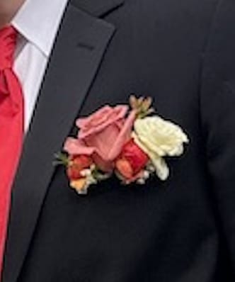 Pink, red, and cream rose boutonniere on a dark suit jacket