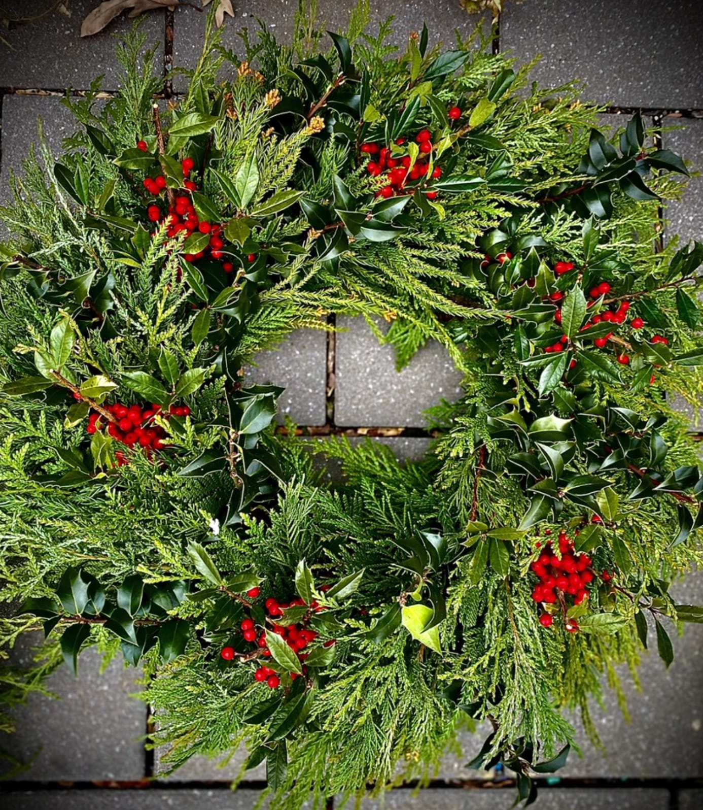 Green holiday wreath with evergreen foliage and red berries on stone pavers