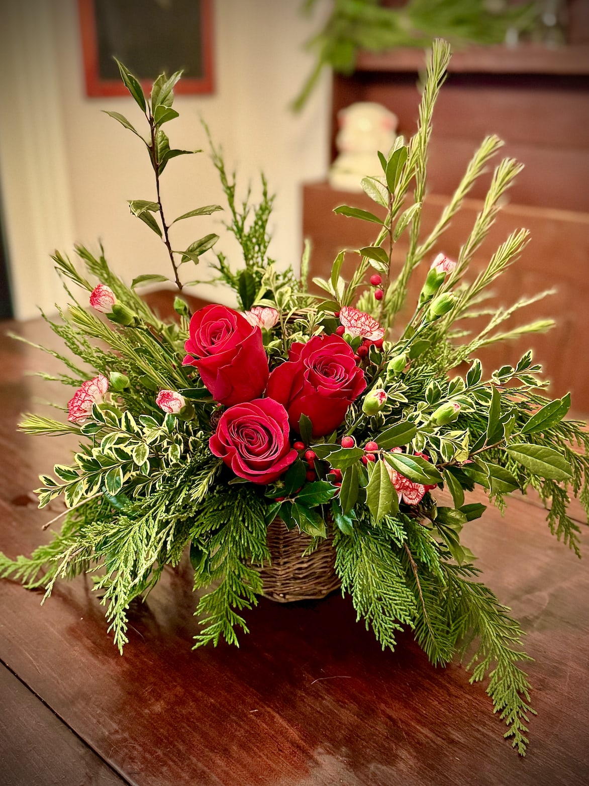 Low basket arrangement of red roses and small pink flowers with abundant evergreen foliage